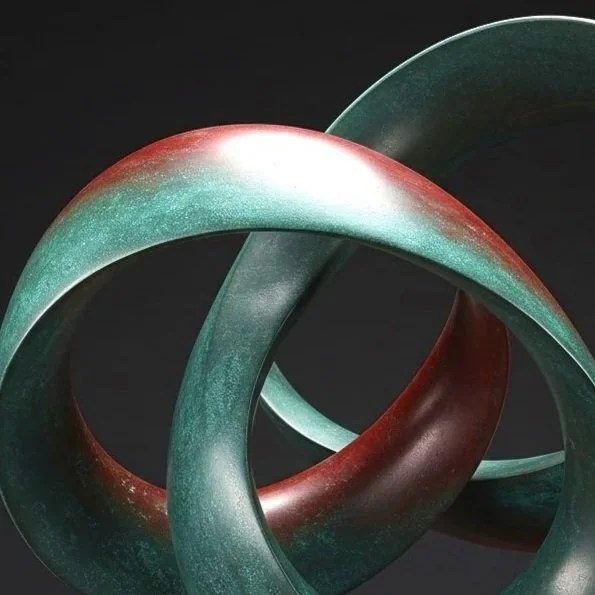 A modern abstract sculpture with intertwined loops, colored in shades of green and red, placed on a gold-colored base against a dark background.