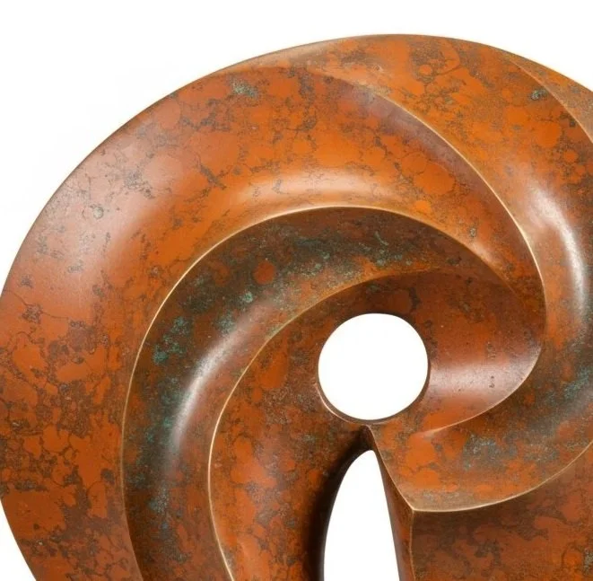 An abstract sculpture made of rusted metal with a circular shape and a spiral cutout, mounted on a wooden base.