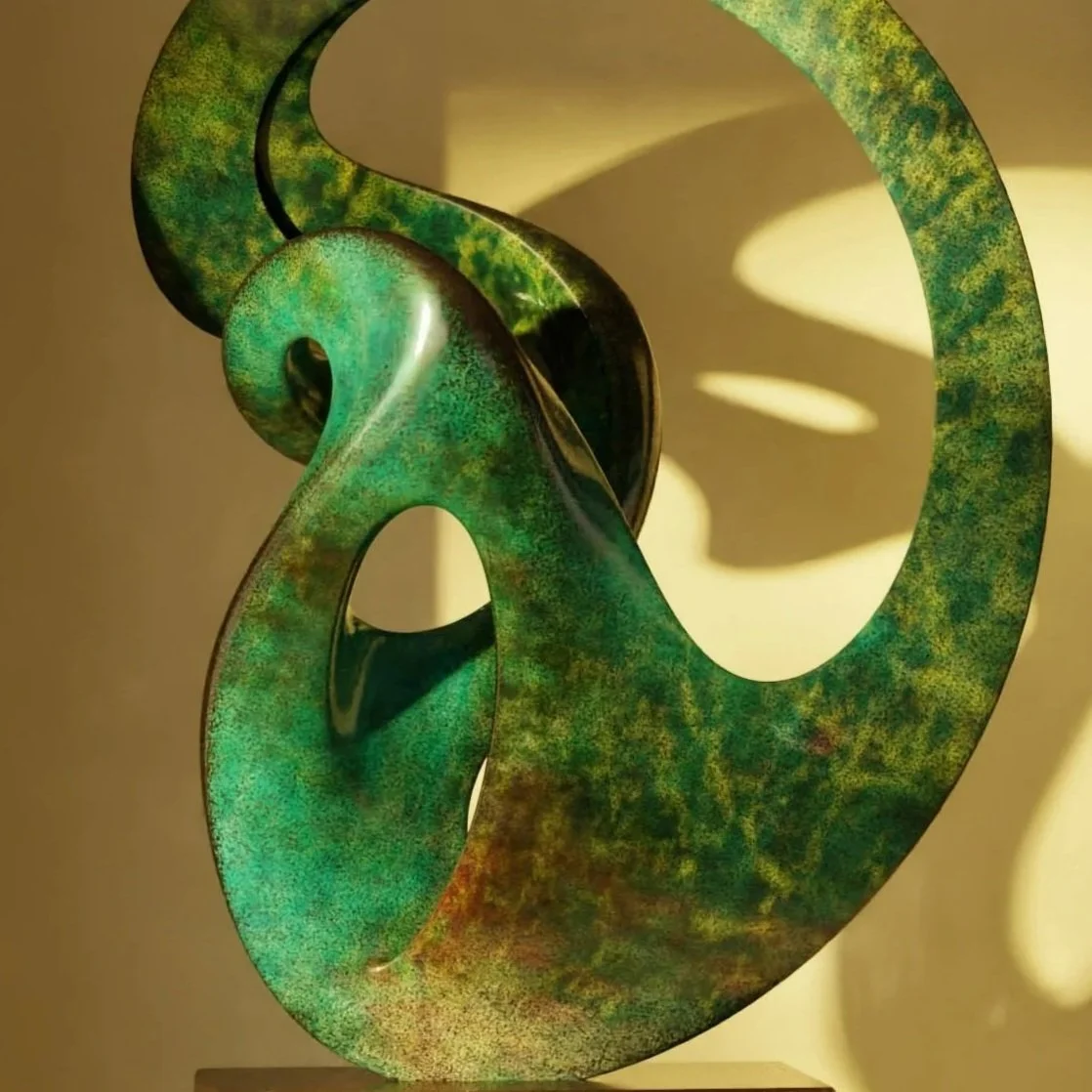 A green abstract sculpture with swirling, flowing shapes cast a shadow on the wall behind it.