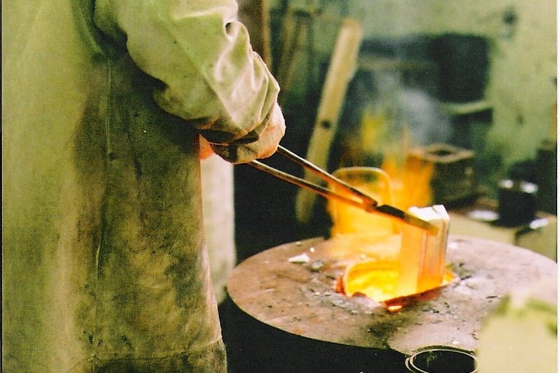 A person wearing protective gloves melting a piece of metal using a blowtorch in a foundry or metalworking shop.