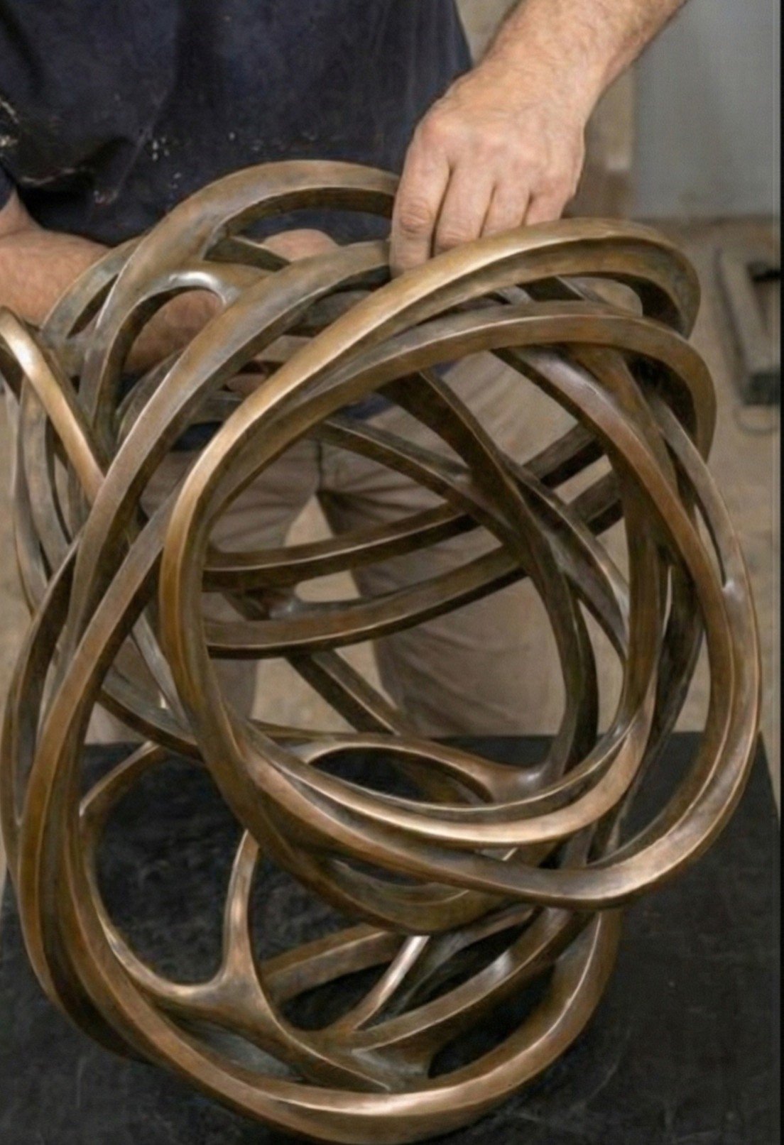 Close-up of a person's hand resting on a large, intertwined wooden sculpture with multiple loops.