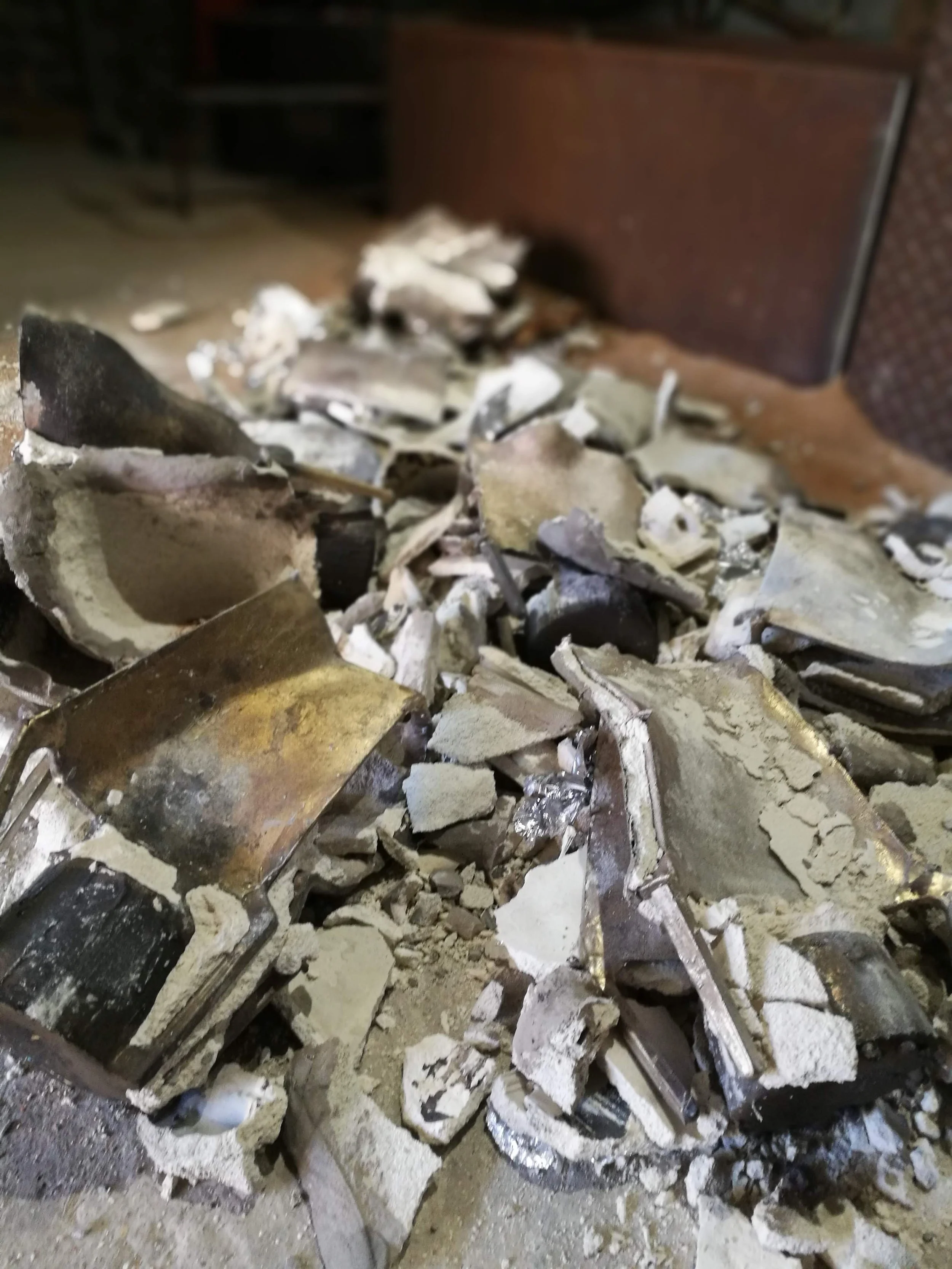 A pile of broken drywall, plaster, and debris on a floor with a piece of black material and a metallic rod visible in the foreground.
