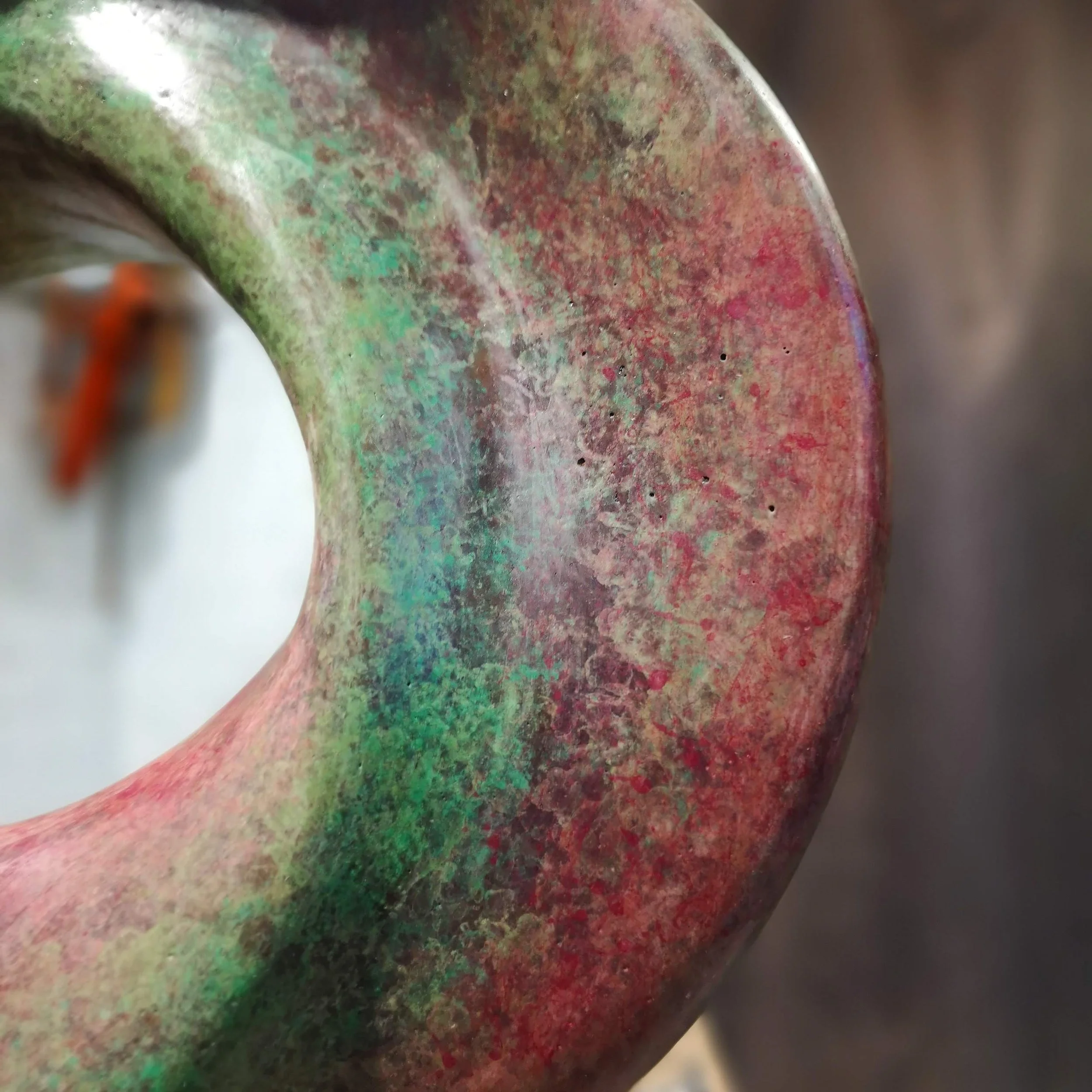 Close-up of a metallic object with iridescent colors, showing green, red, and purple hues, with a smooth, rounded surface.