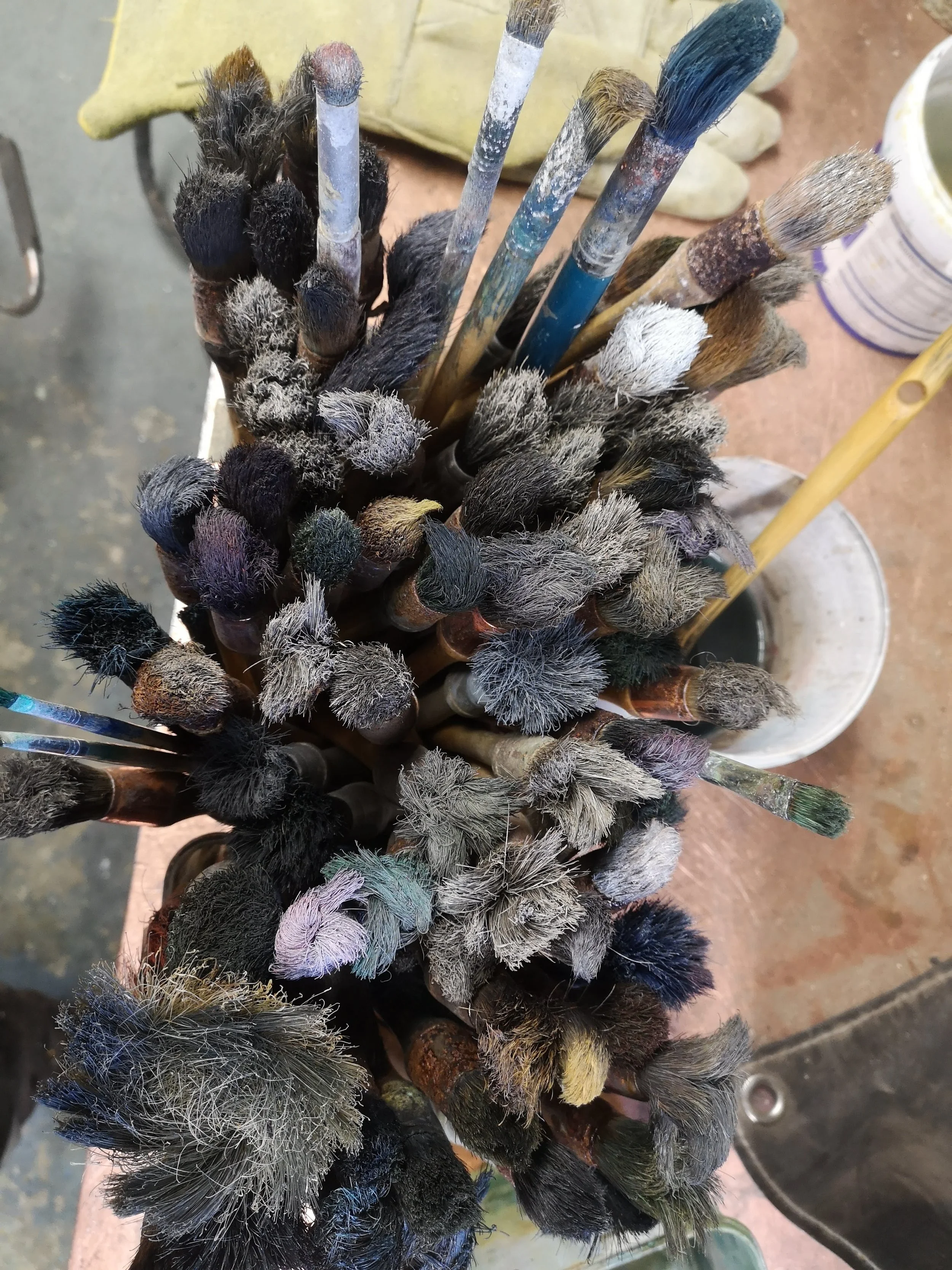 Close-up of many old paintbrushes with frayed bristles and paint stains, bundled together and leaning in a container.