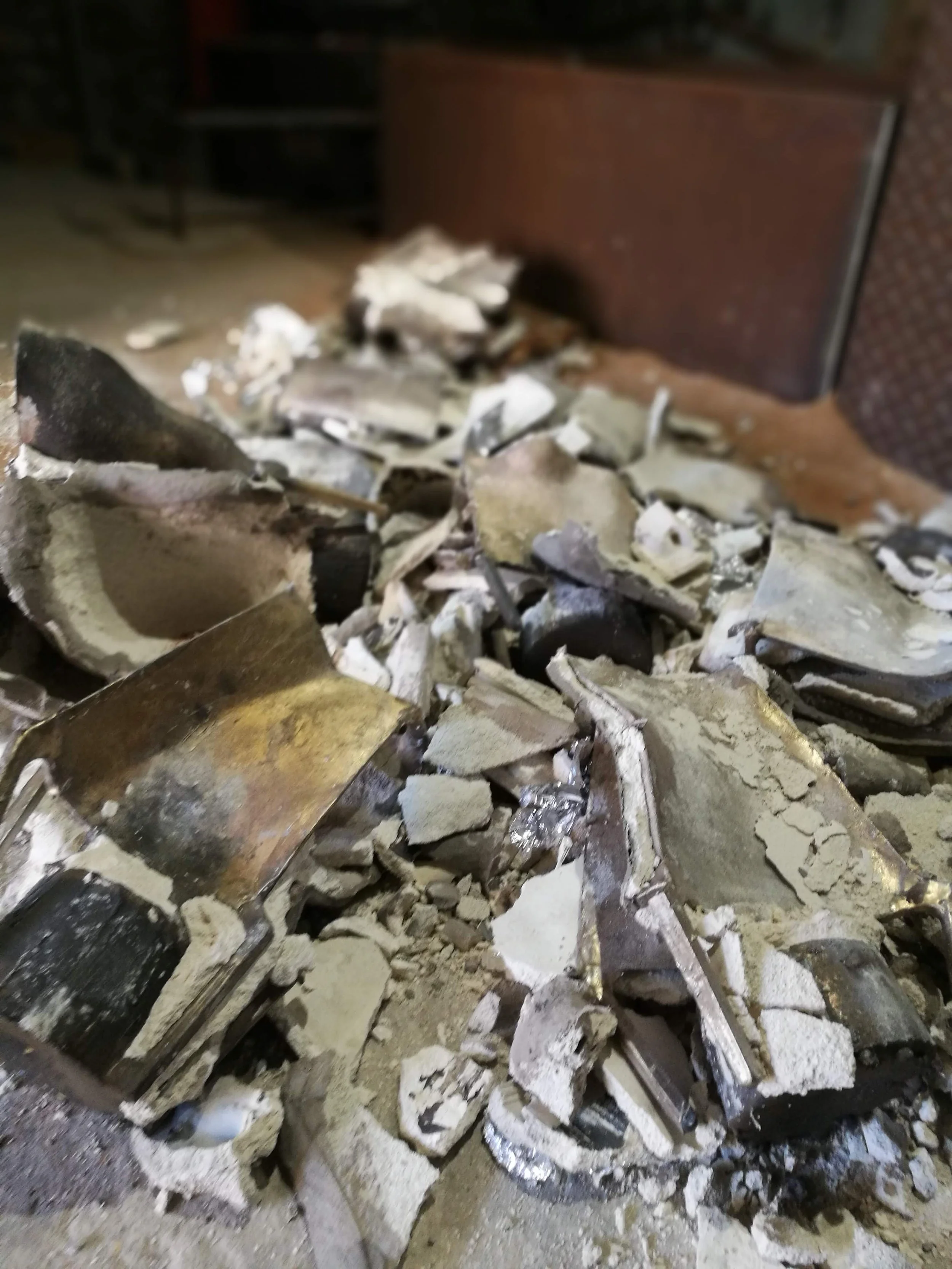 Broken and charred metal and debris, possibly from a burned object or structure, on the ground near a brown brick wall.