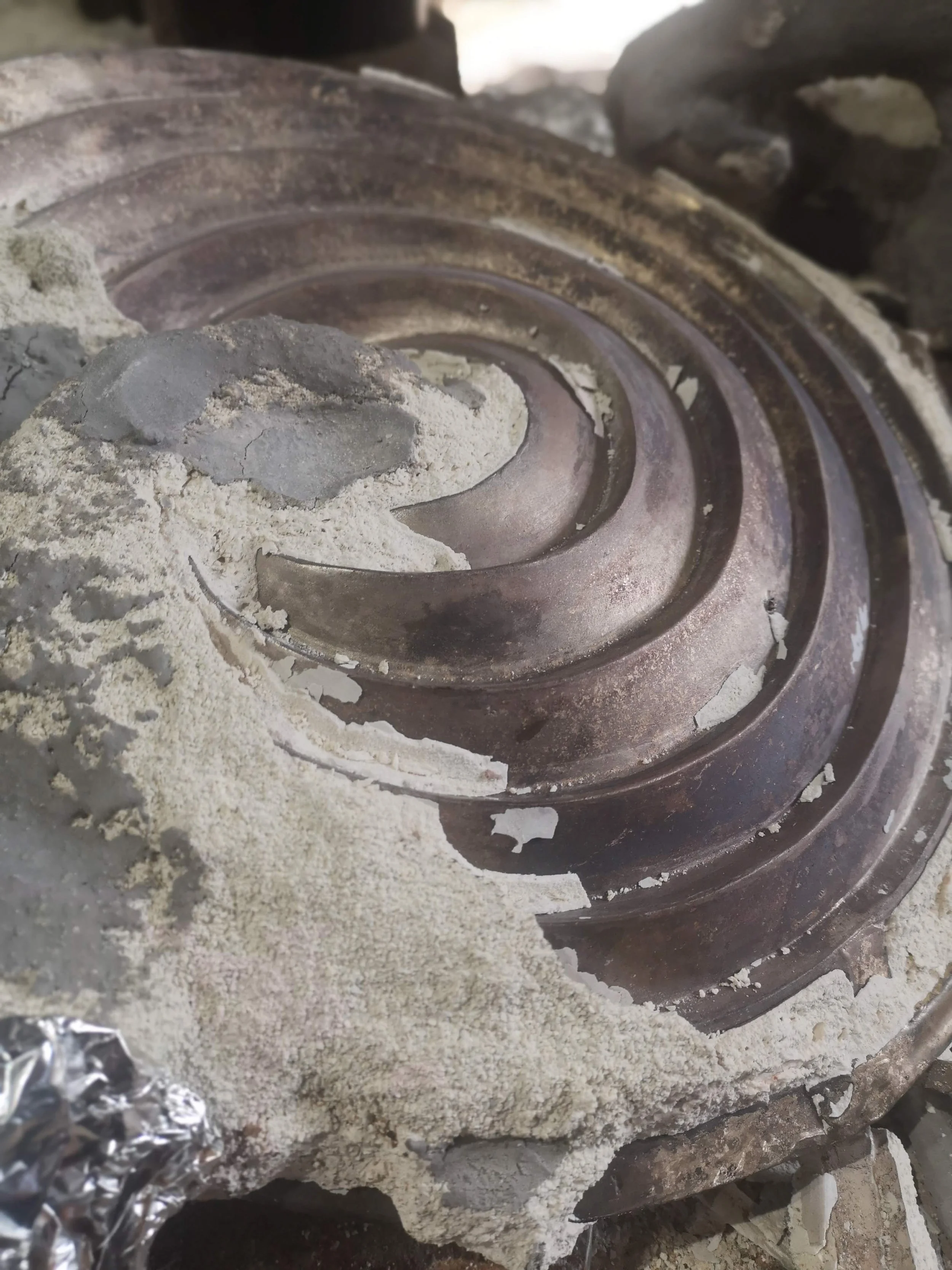 Close-up of a large, rusty bearing surrounded by dusty concrete and crumpled aluminum foil.