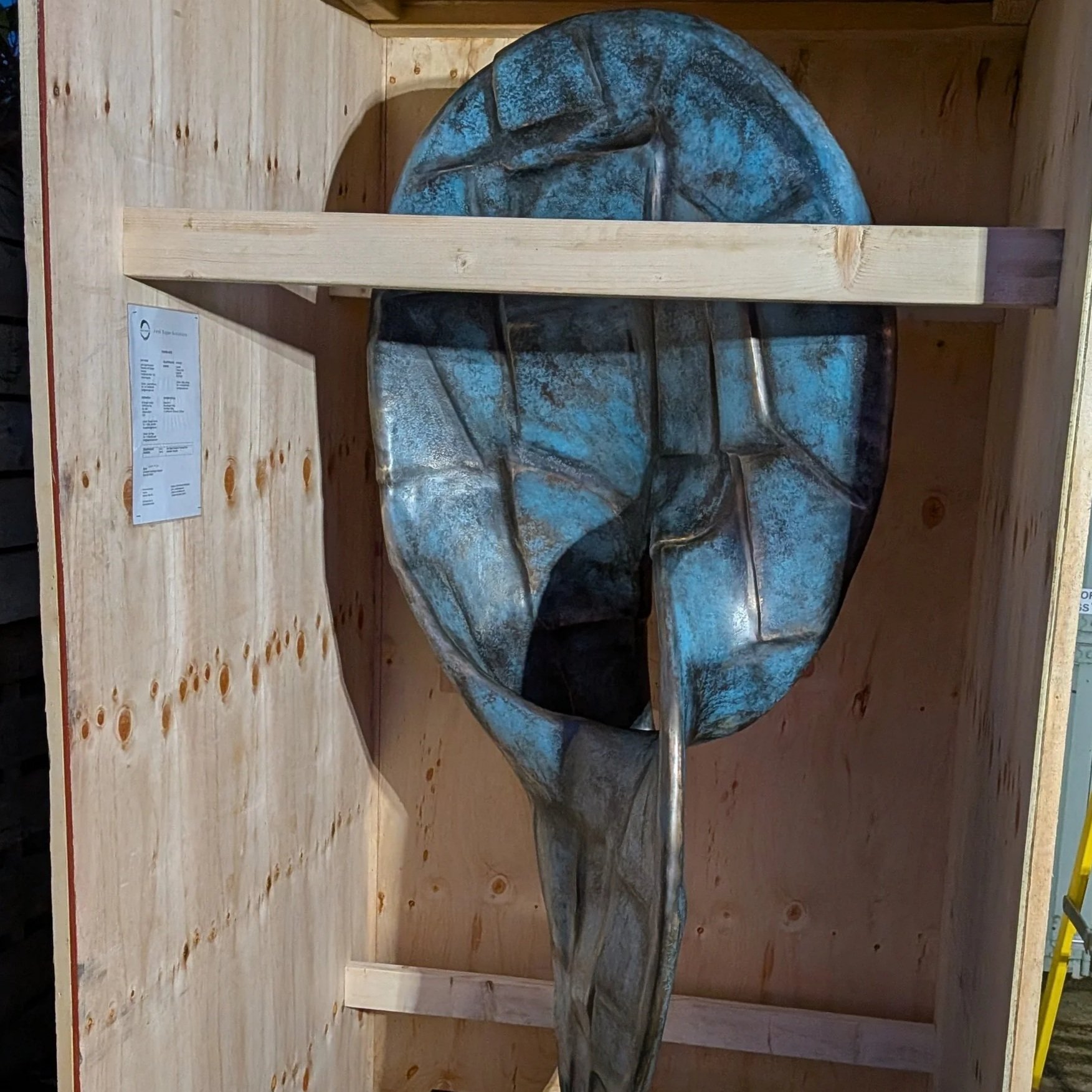 Metal sculpture of an abstract face with blue and gray tones, displayed on a wooden platform.
