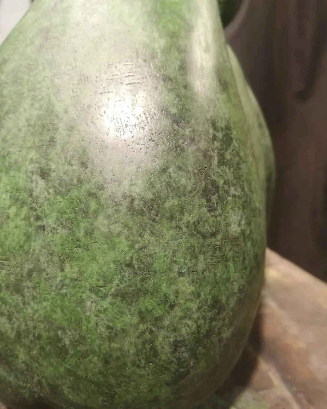 Close-up of a weathered, greenish metallic surface with patches of rust and scratches, likely part of a vintage object or sculpture.