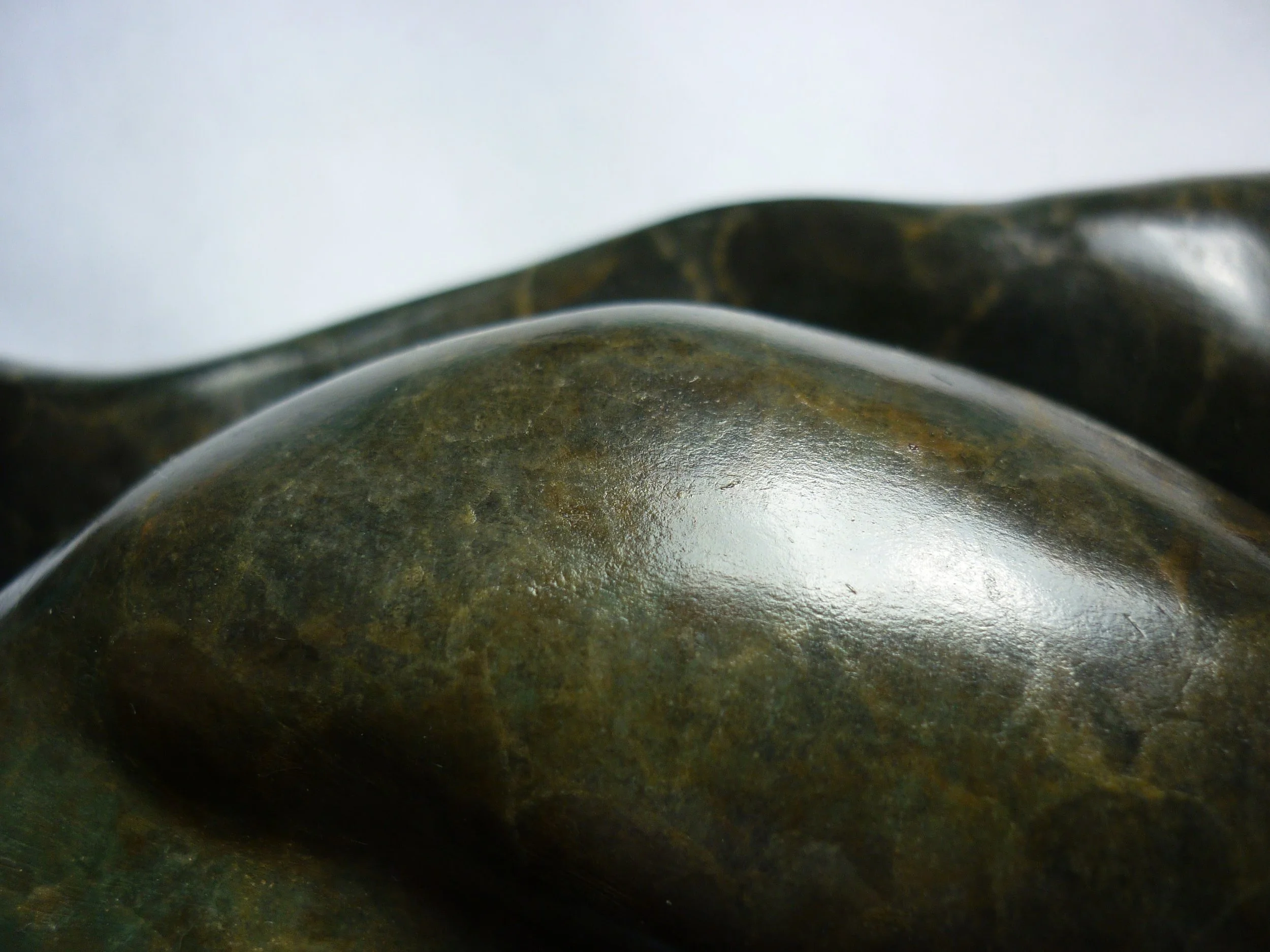 Close-up of smooth, rounded, dark-colored stones with some greenish and brownish hues.