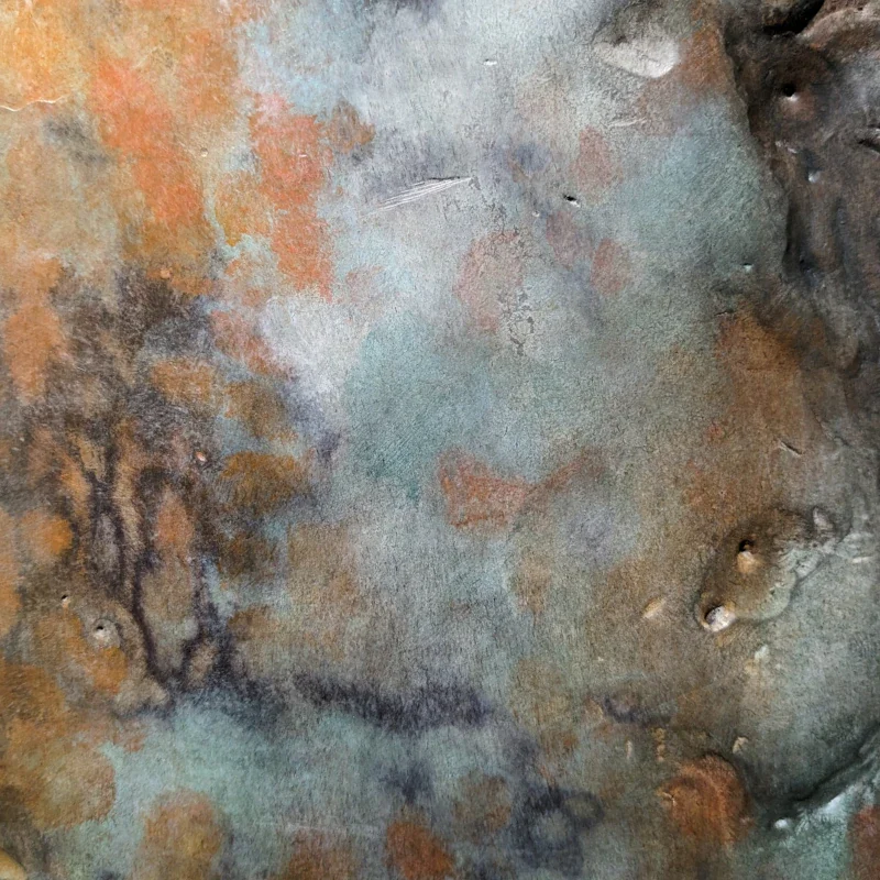 Close-up of a textured, weathered metal surface with rust and patina in shades of orange, blue, and brown, featuring areas of corrosion and small dents.