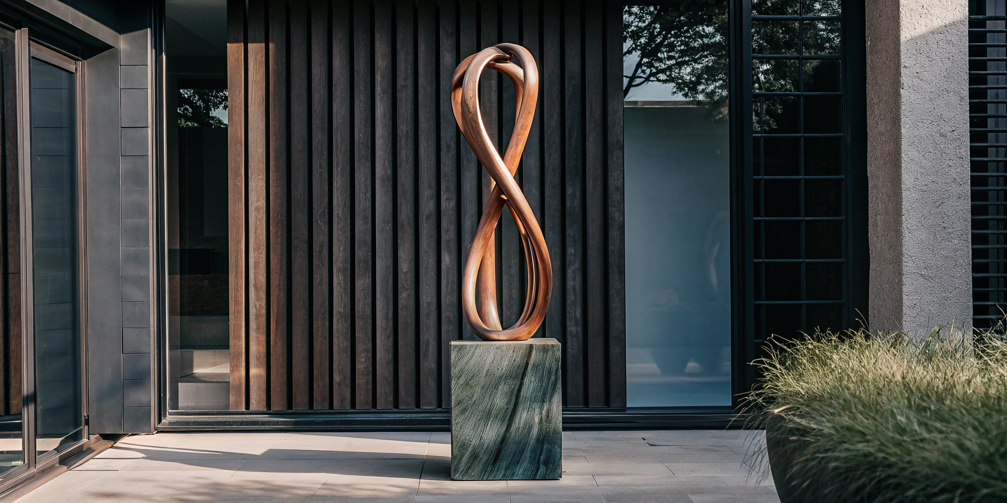 Modern building exterior with vertical black wooden panels, large glass window, and a bronze abstract sculpture on a square base.