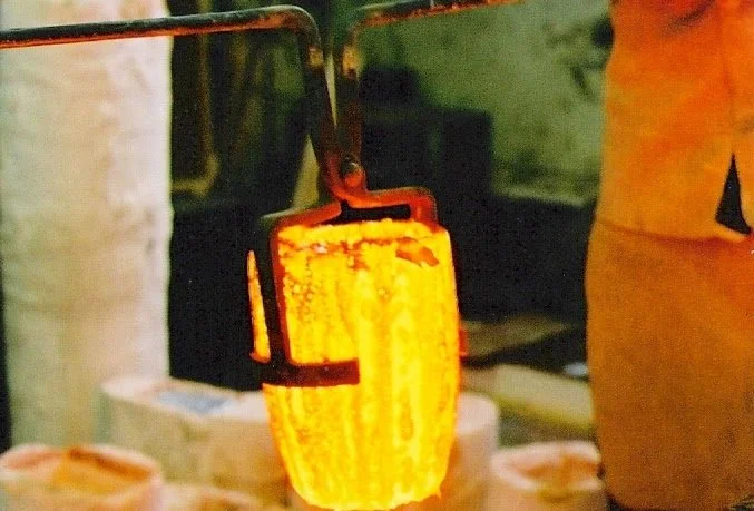 Close-up of a person holding a heated melting pot or taffy cutter over a table, with a yellow-orange glowing substance, likely caramel or candy.