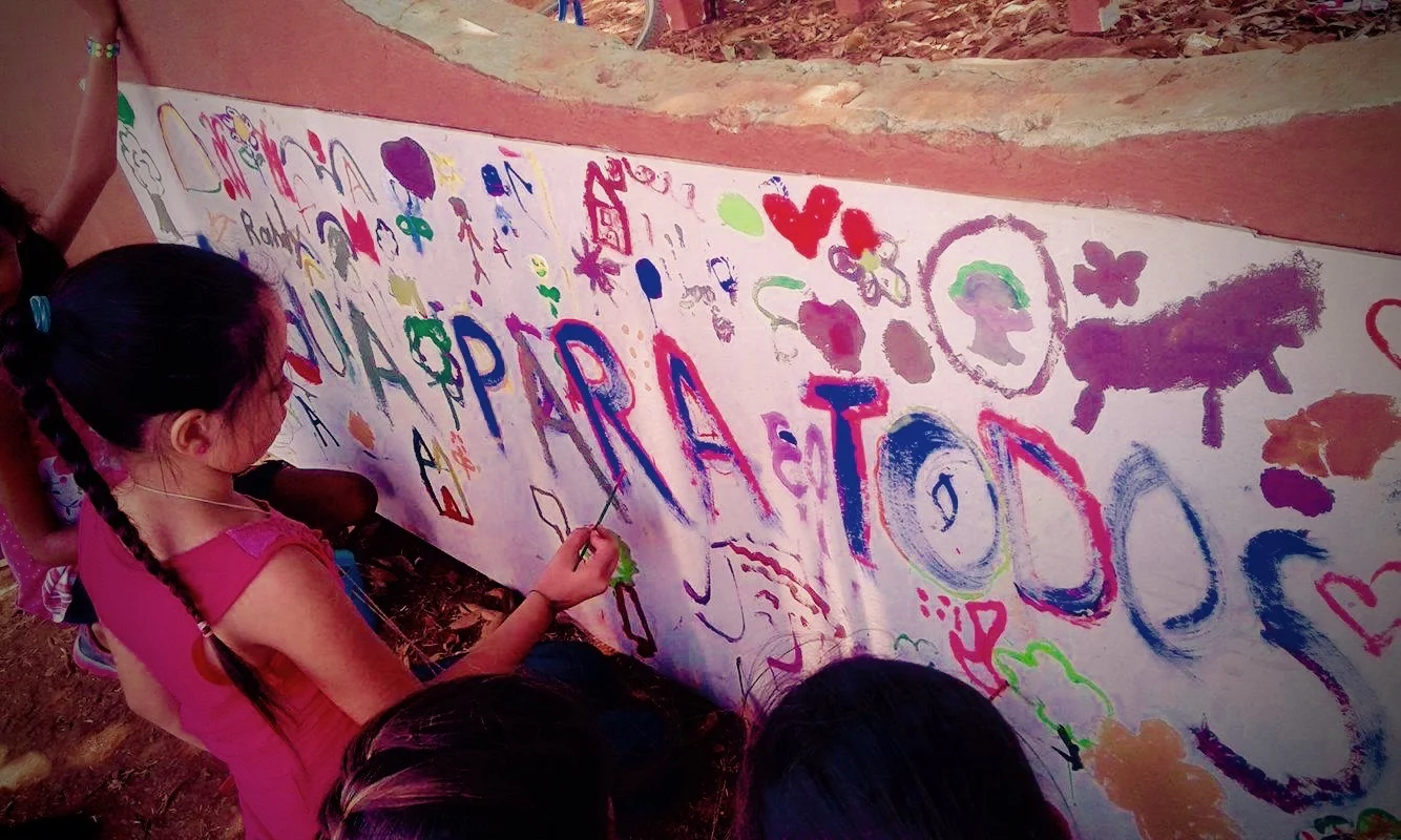 Kids painting a mural that says "Agua Para Todos" or water for everyone. 