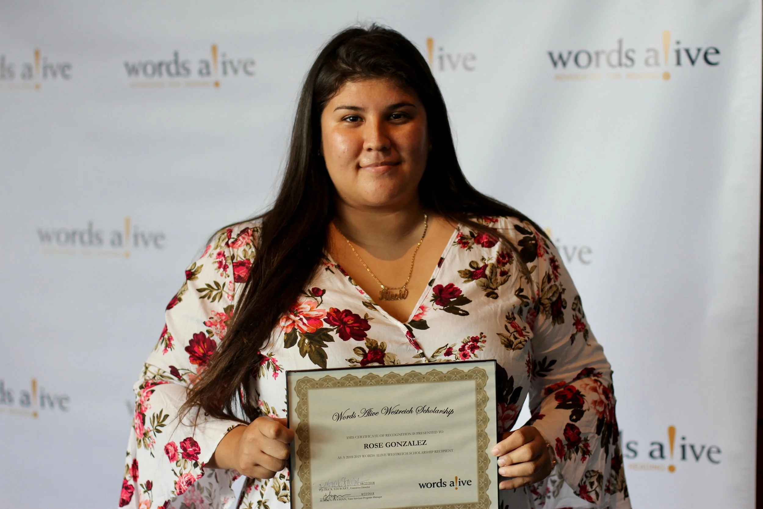 An image of Rose Gonzalez holding her award in front of a Words Alive backdrop.
