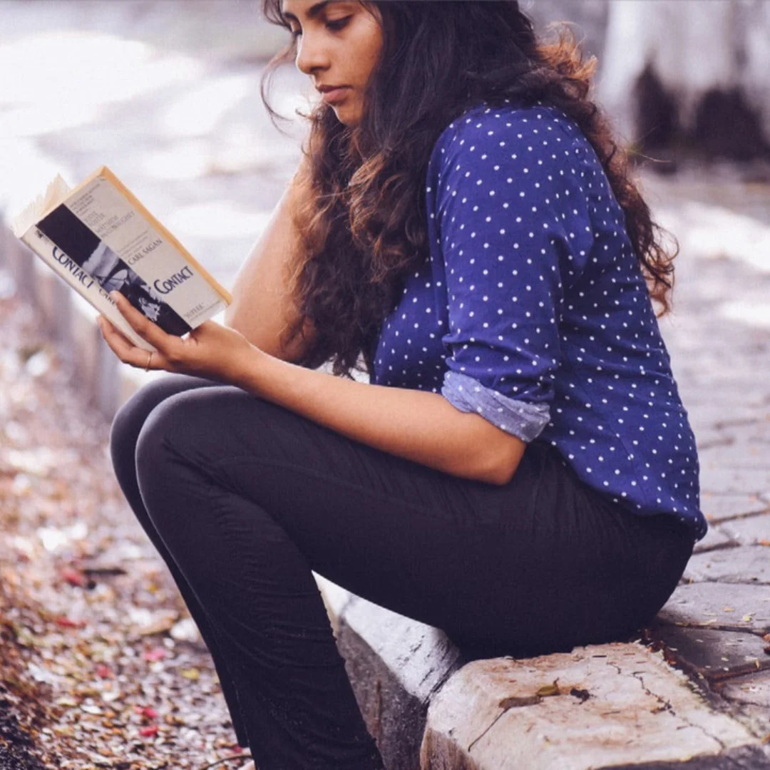 Image of a young person sitting on the sidewalk and reading Contact.
