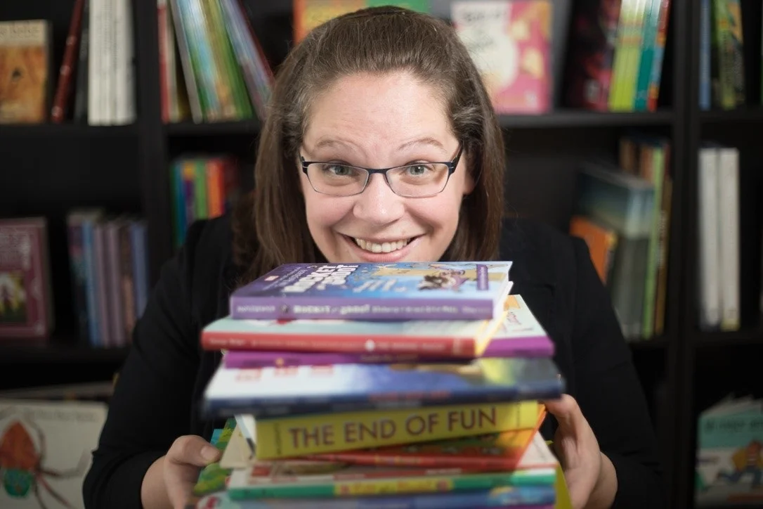 An image of Rachael looking at the camera and smiling while she holds a stack of books!