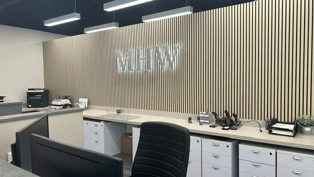 Dimensional metal MHW logo letters installed on a modern slatted office wall