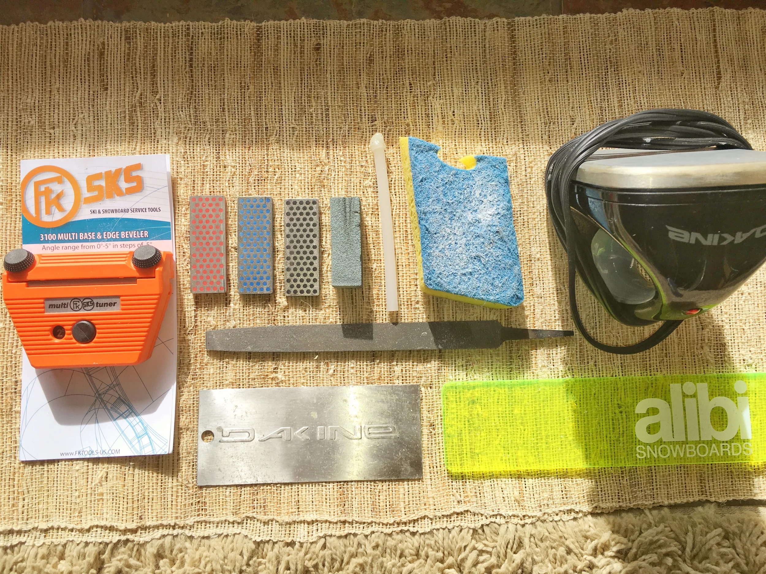 Top left to right: tuning side/base edge tool with file inserted, diamond stones (fine, medium, course), gummy stone, p-tex stick, nylon scourer, waxing iron. Middle: medium-cut file. Bottom left to right: metal scraper, plastic scraper.