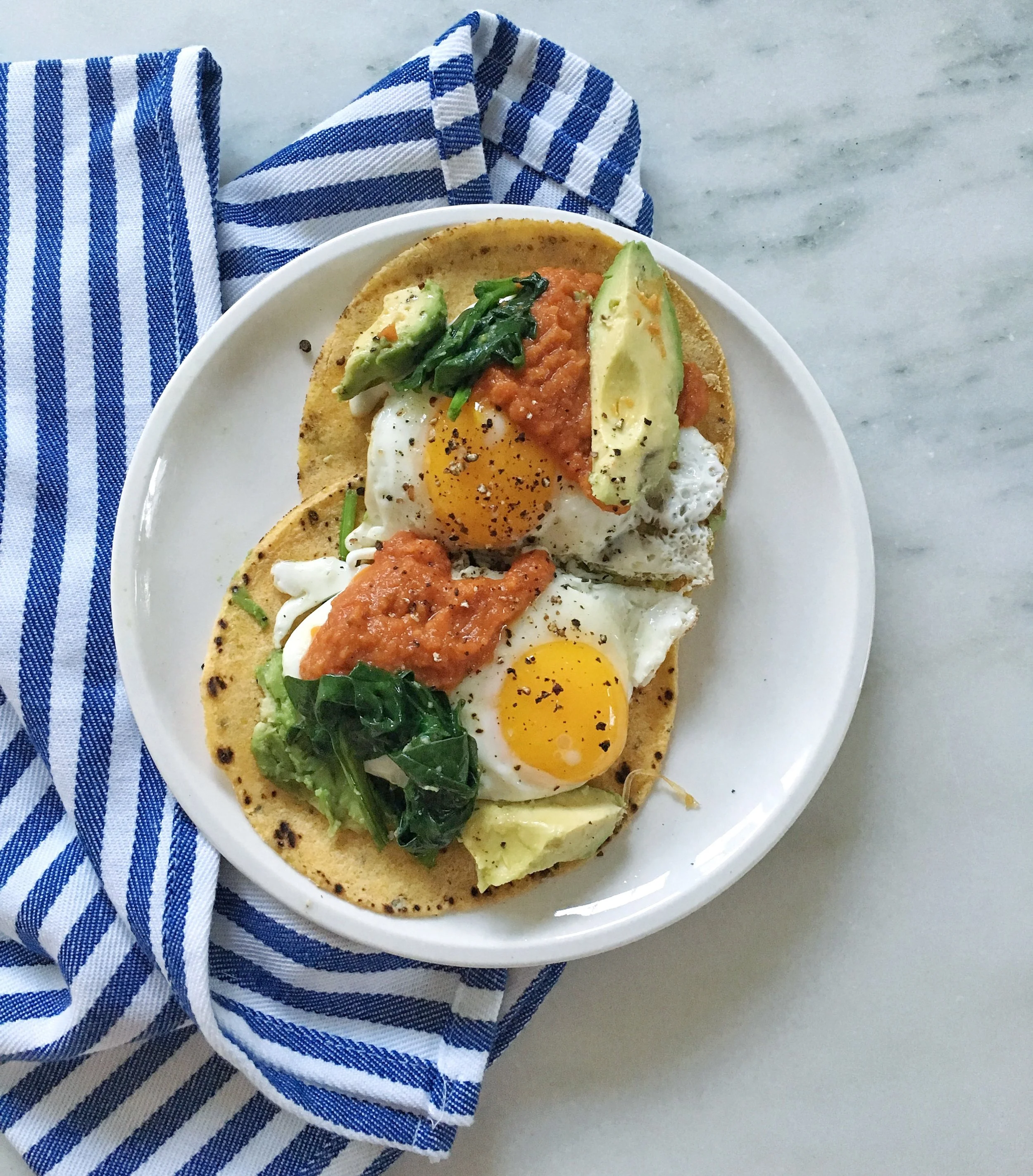 Corn tortillas with fried eggs, sautéed spinach, avocado, tomato everything sauce, salt and pepper