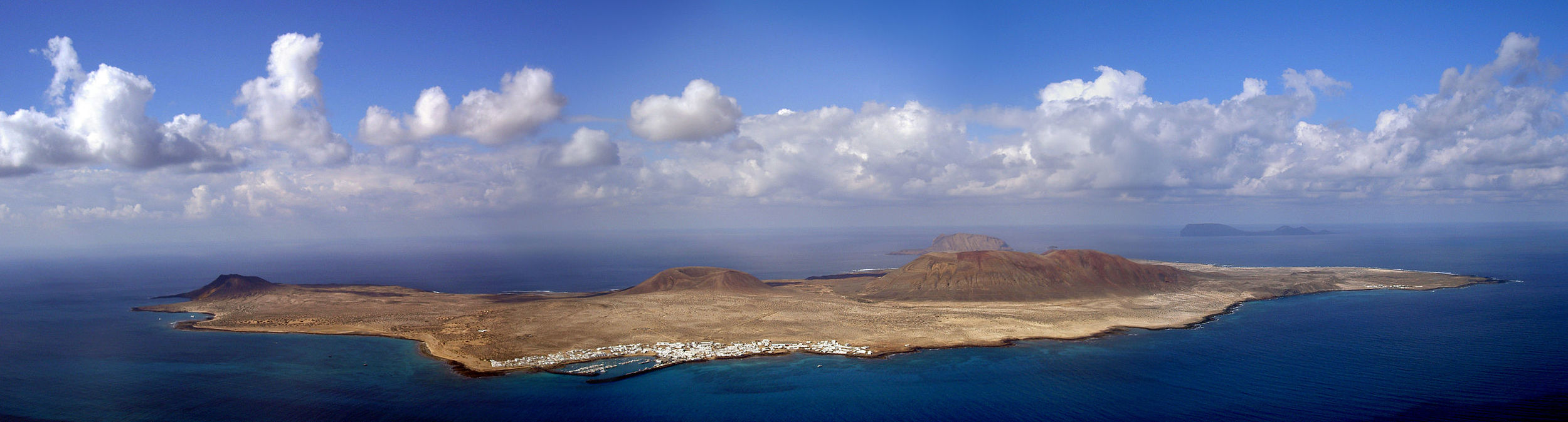 Bild oben: Blick vom Mirador del Rio hinunter auf die Insel La Graciosa. Vorne der Hafen und das Dorf Caleta de Sebo, im Hintergrund am Horizont die Inseln Montaña Clara und Alegranza.