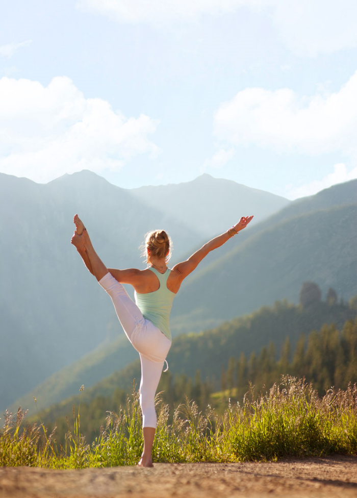 A lady doing Utthita Hasta Padangustasana pose in the mountains.