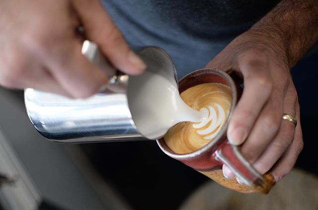 Pouring steamed milk into ceramic mug to make a latte