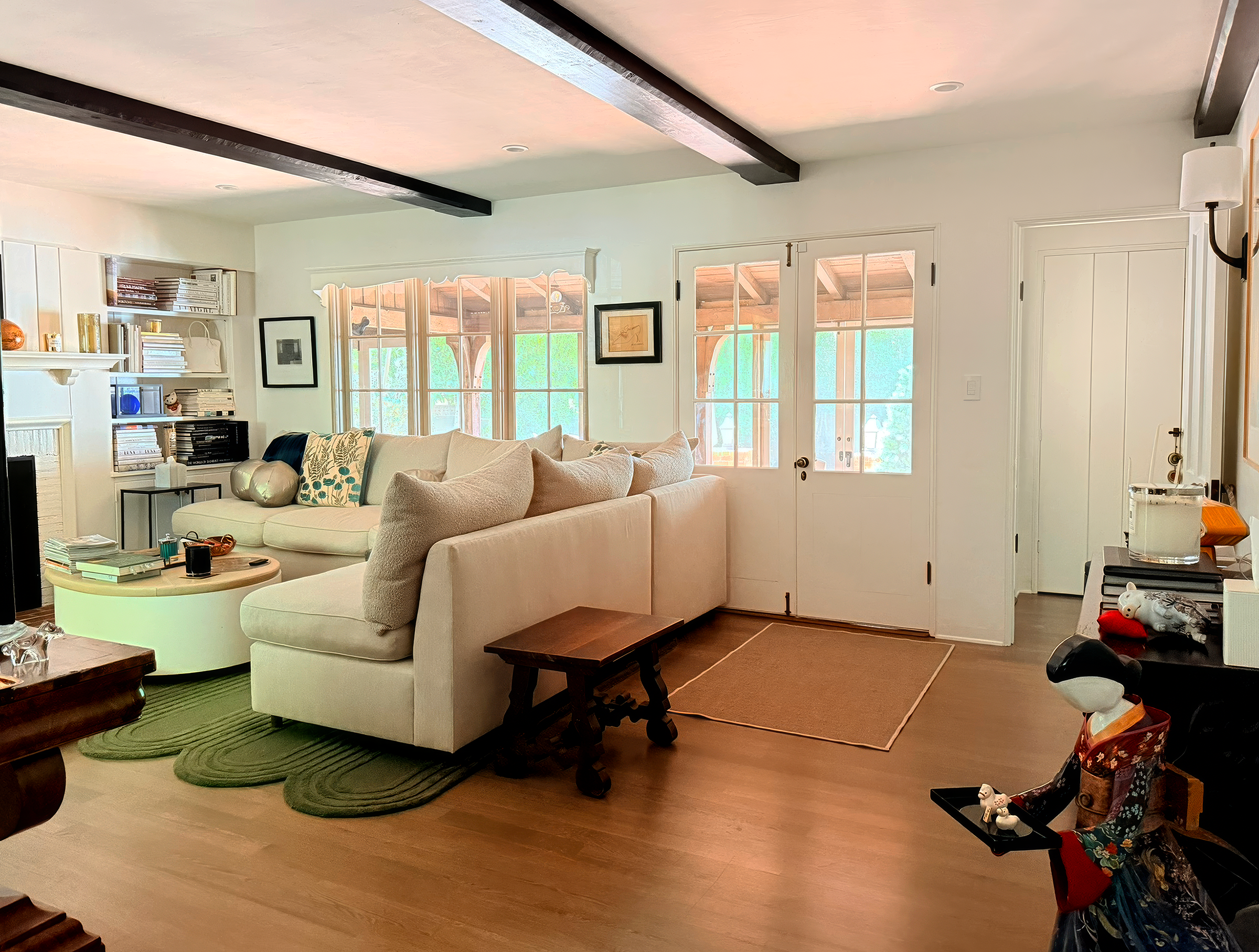 Living room with white walls, a beige sofa, small round coffee table, bookshelves, and large windows with wooden frames.