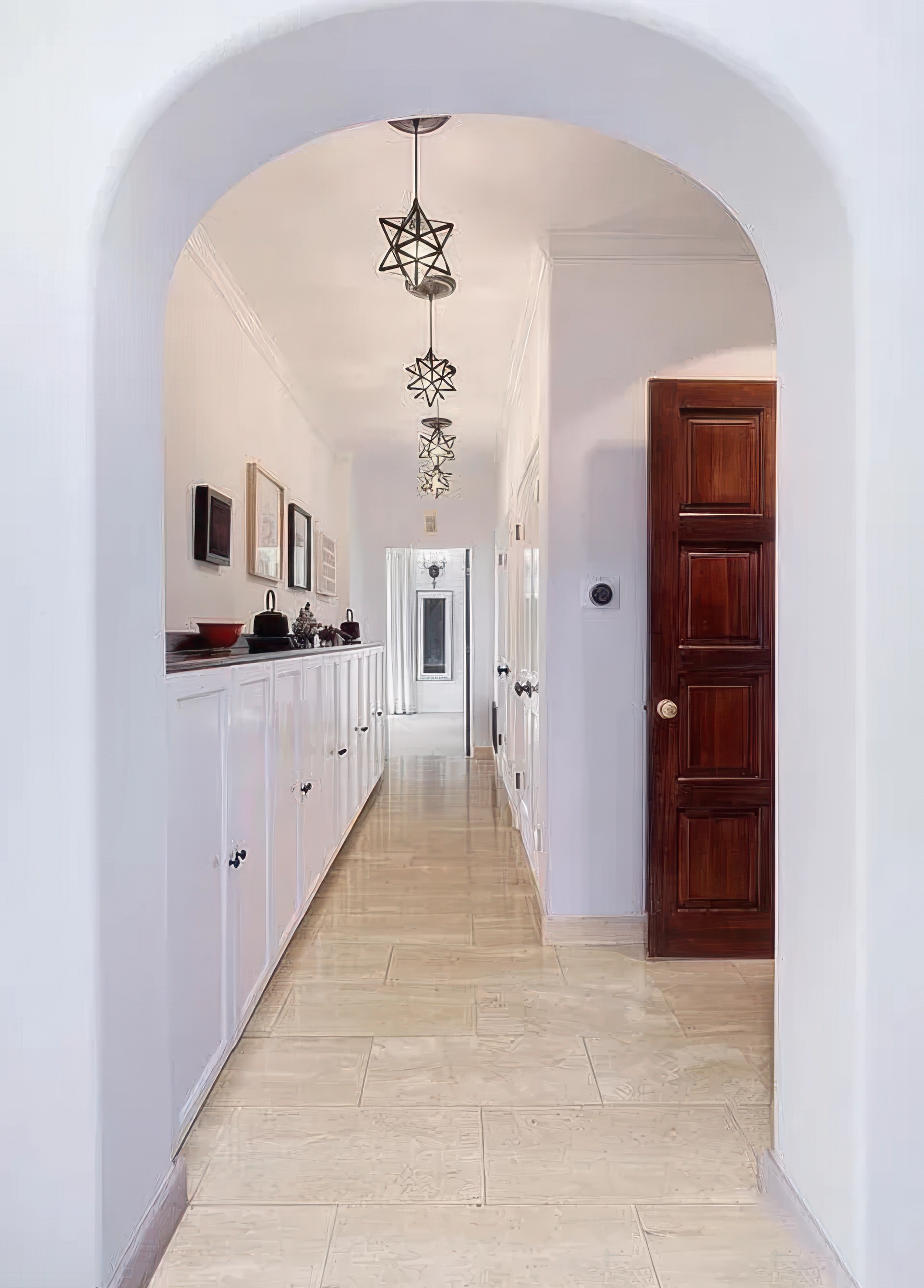 Long hallway with white walls, wooden floor, and decorative hanging lights shaped like stars. Wooden door on the right side, and framed pictures on the left wall leading to a door at the end.