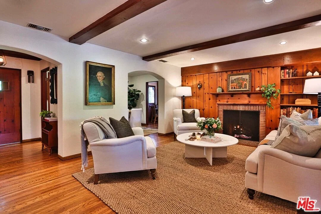 Living room with white sofas, a round coffee table with flowers, a wood-paneled fireplace, and a painting on the wall.