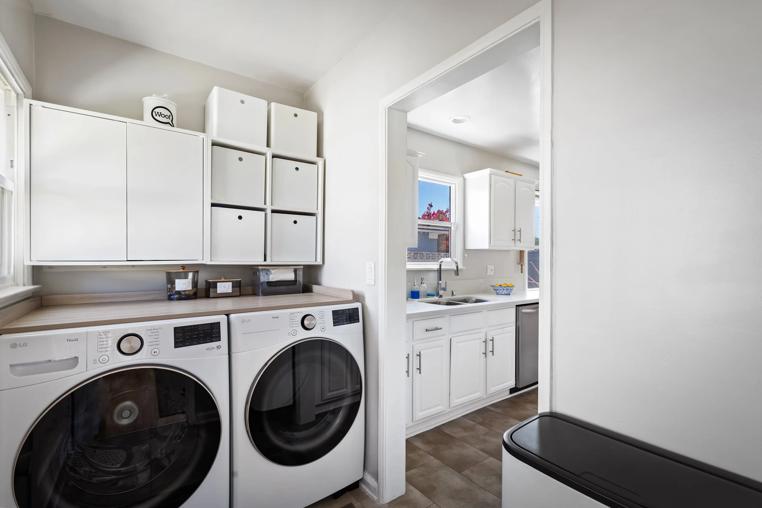 Laundry room with white cabinets and a window with pink flowers outside, a sink, and a washer and dryer.