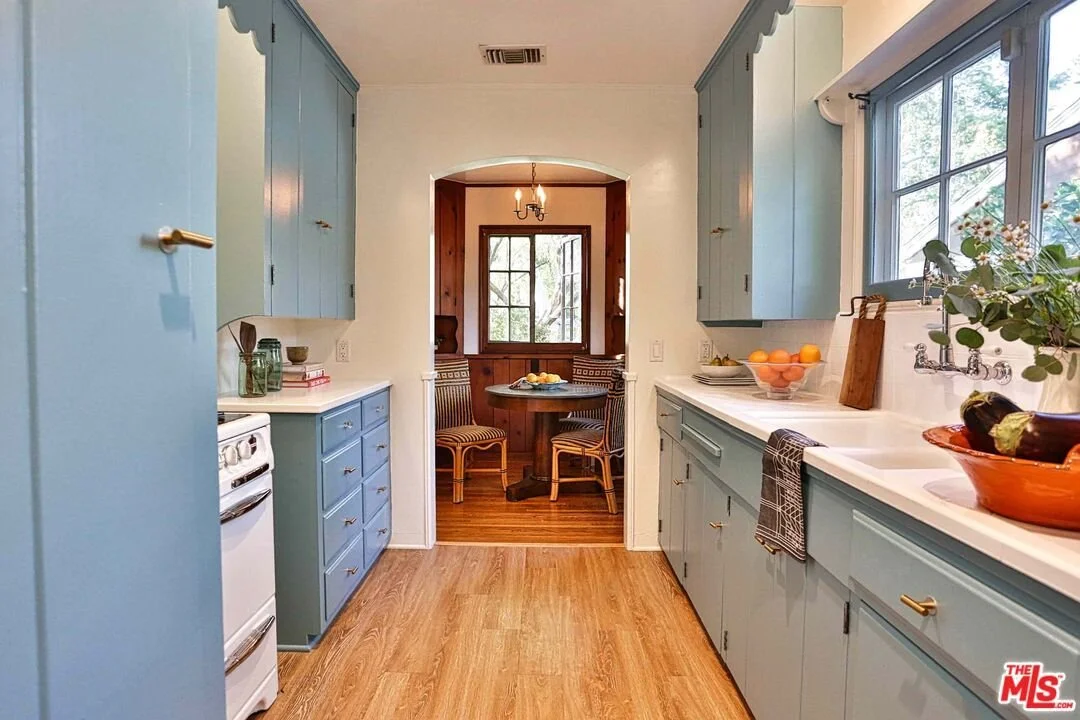 Kitchen with light blue cabinets, white countertop, window above sink, and a small dining nook with wood paneling and a round table with four chairs.