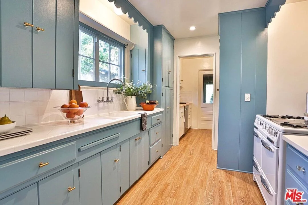 Kitchen with blue cabinets, white countertops, a window above the sink, a bowl of eggs, and a white stove.