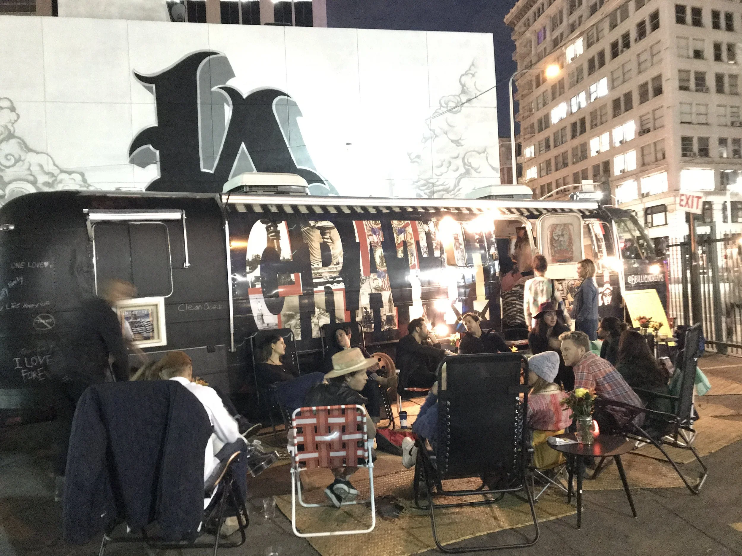 Group of people sit in folding chairs around the Gratitude Bus in the city. 
