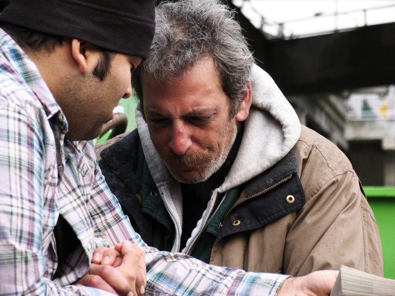 A young man prays with a homeless man. 