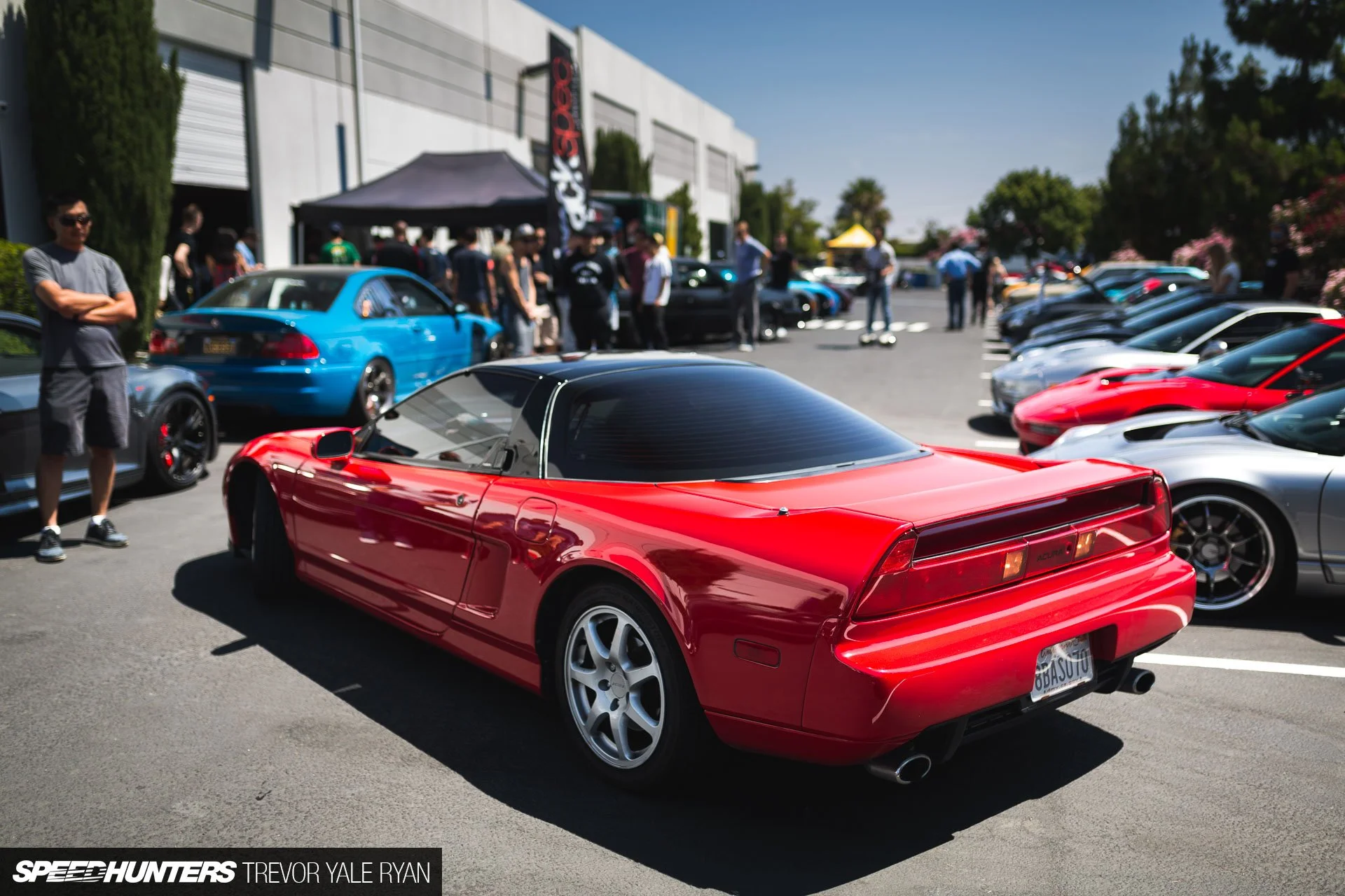 Red sports car parked among other cars at a car show, with people walking and sightseeing in the background.
