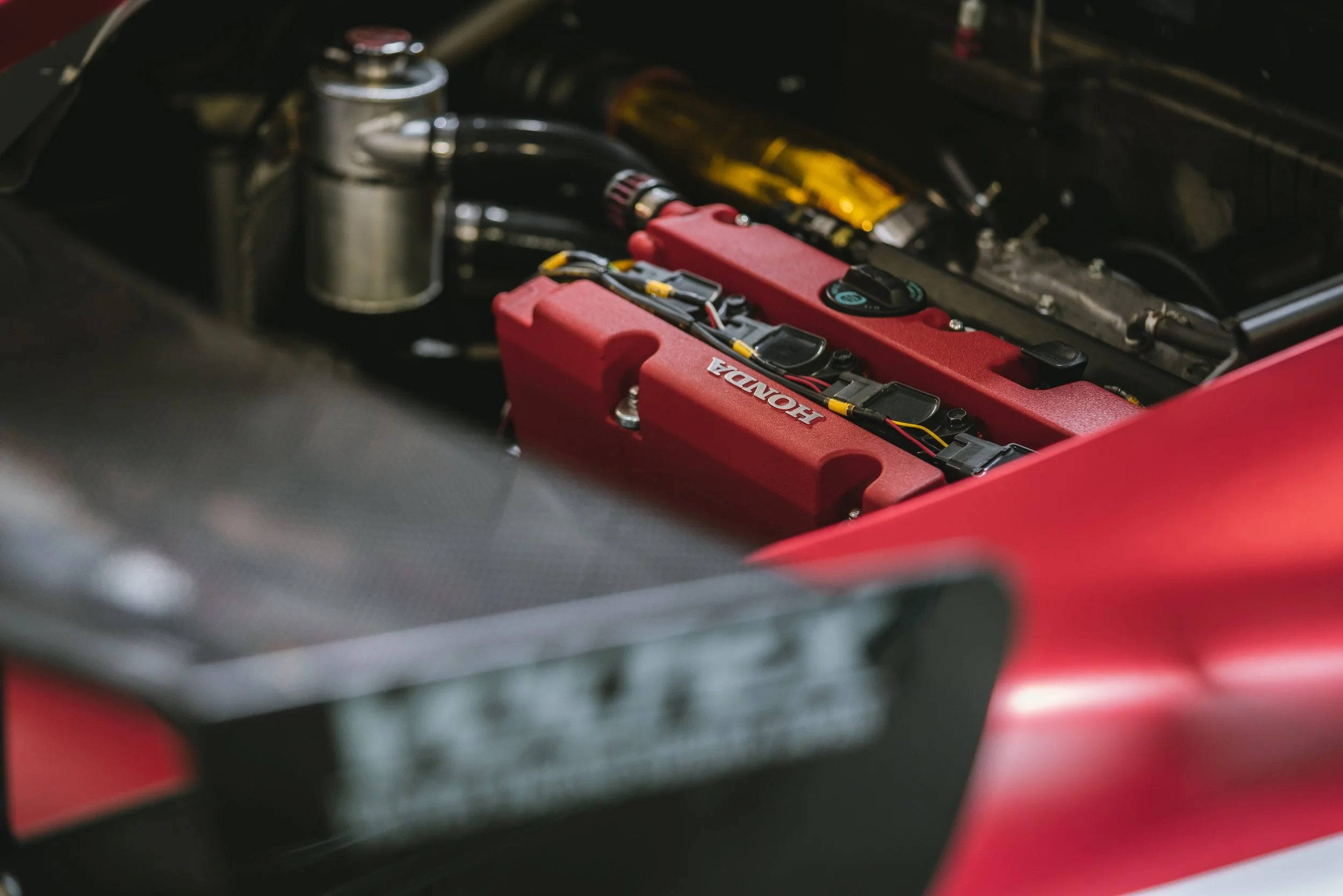 Close-up of a Honda engine with a red valve cover in a car engine bay.