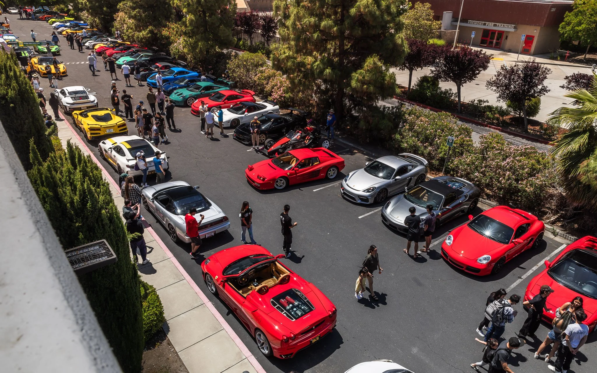 A parking lot filled with various colorful sports cars and people walking around, at an event near Fremont Fire Training.