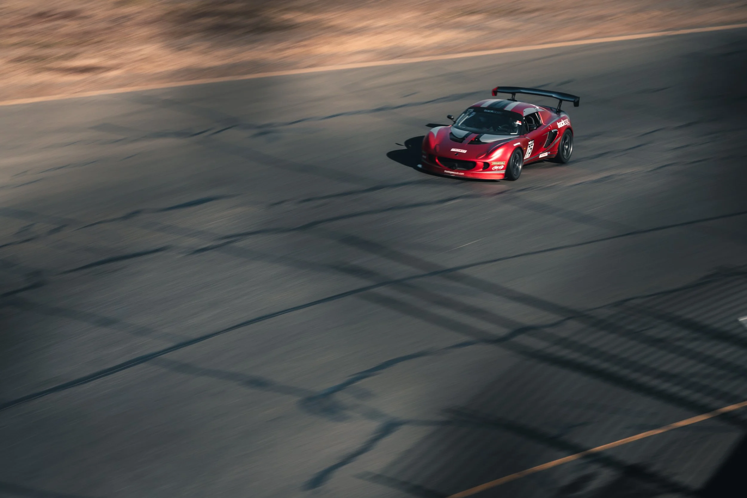 Red race car speeding on a track with shadows of fencing overhead.