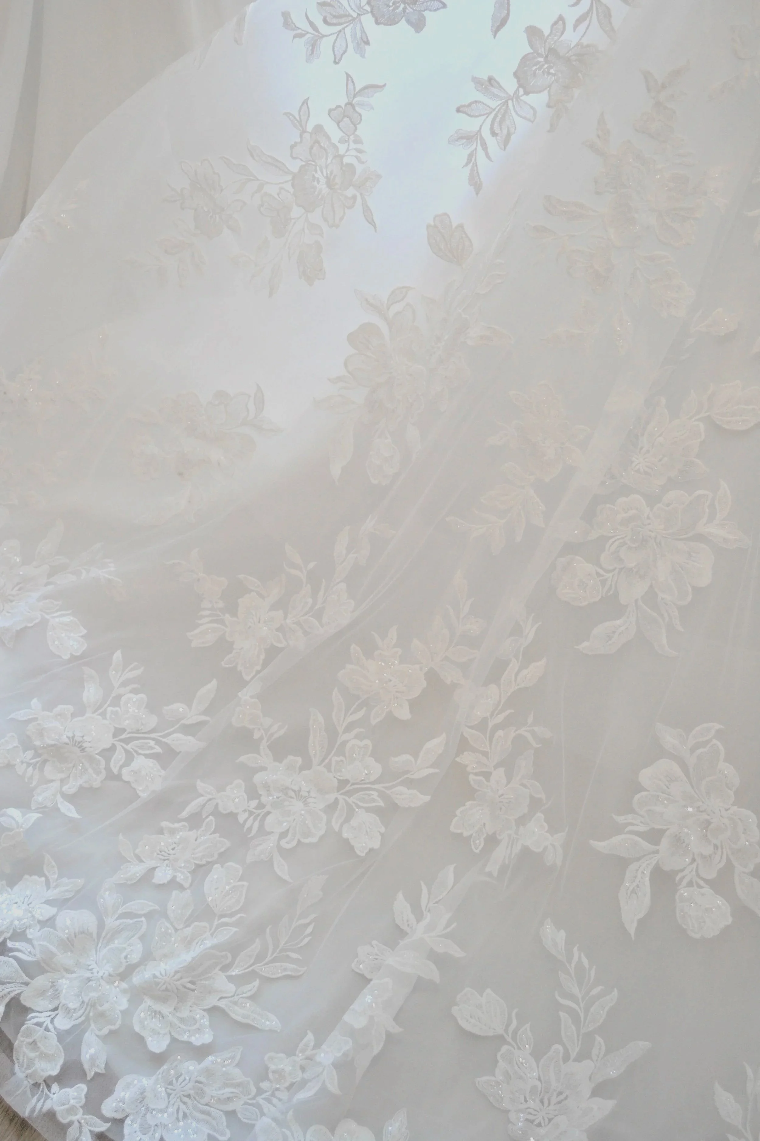 Close-up of a white lace fabric with floral embroidery and a sheer overlay.