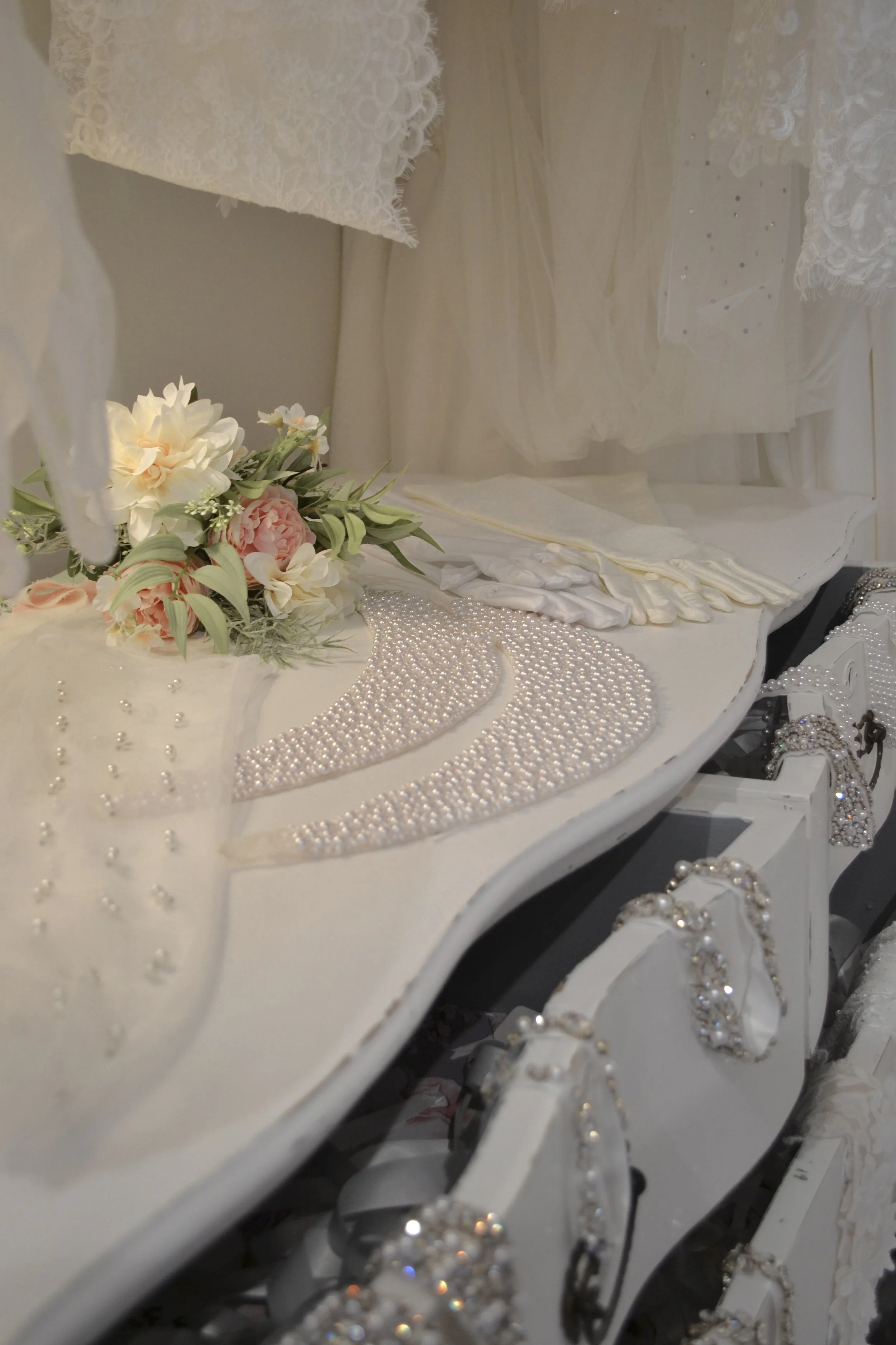 Decorative white dresser with pearl embellishments, a floral arrangement with pink and white flowers, and jewelry accessories including earrings and pearl necklaces.