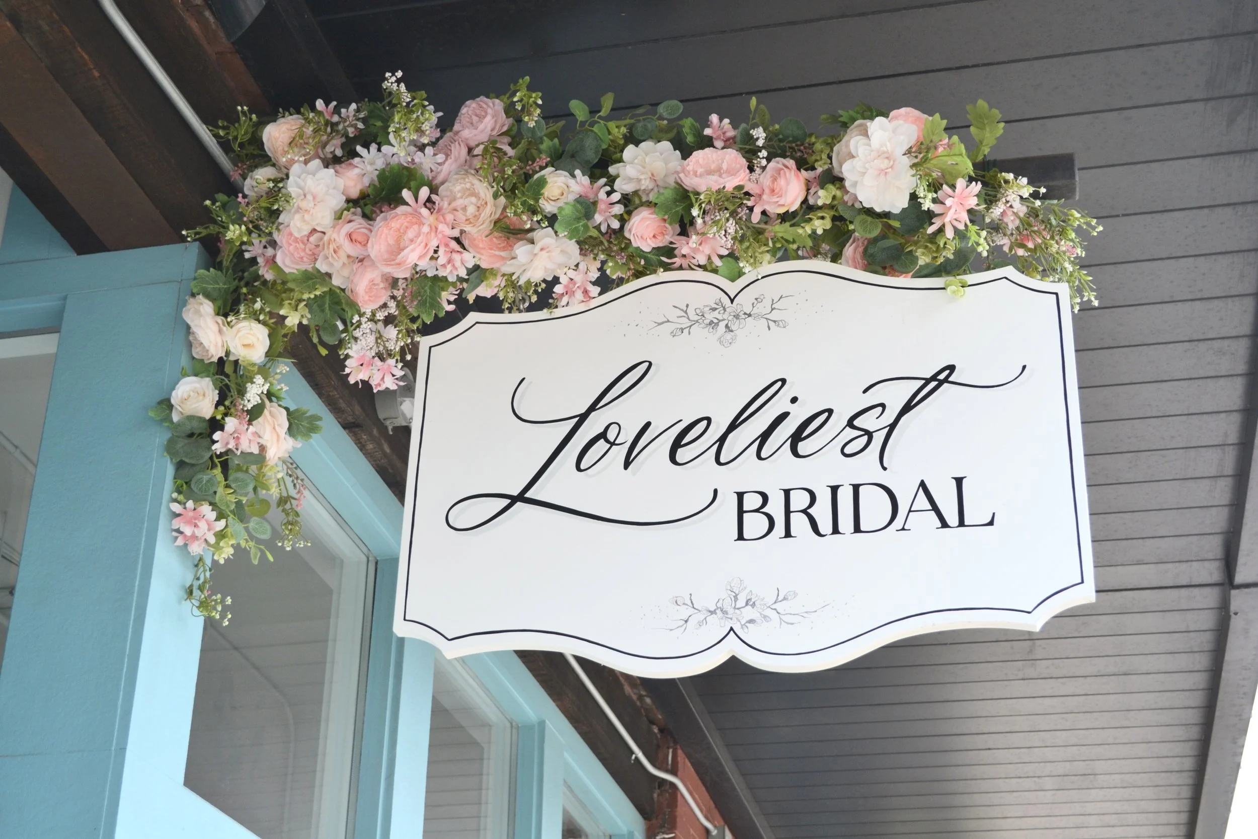 A floral wedding arch with pink and white flowers above a white sign that reads 'loveliest bride'.