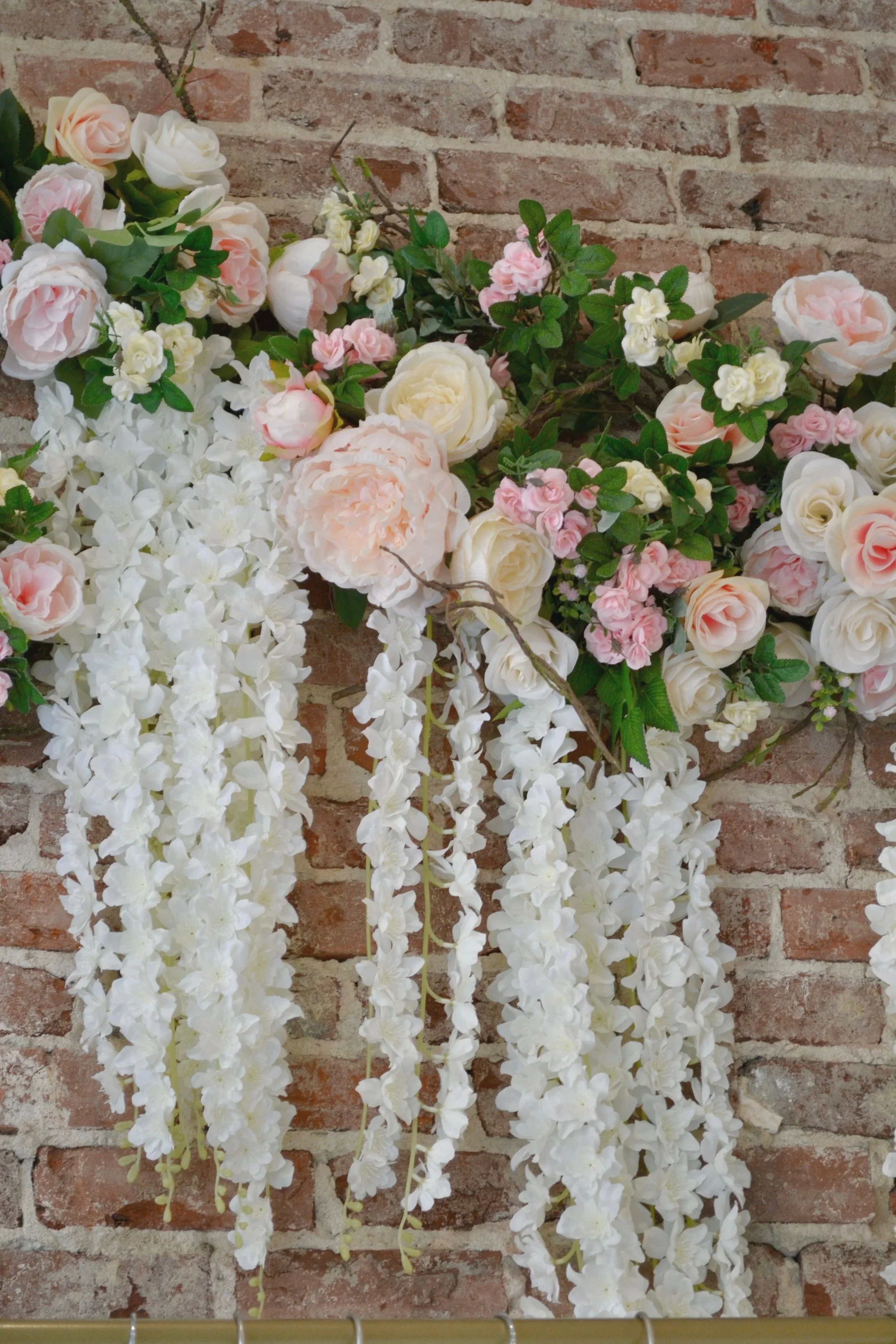 A wall of brick with hanging artificial white and pink flowers, some with green leaves.