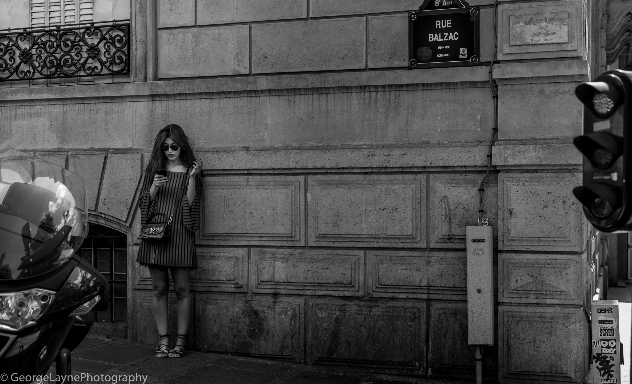 A lady smokes and checks her phone on a street next to the Champs Élyées.