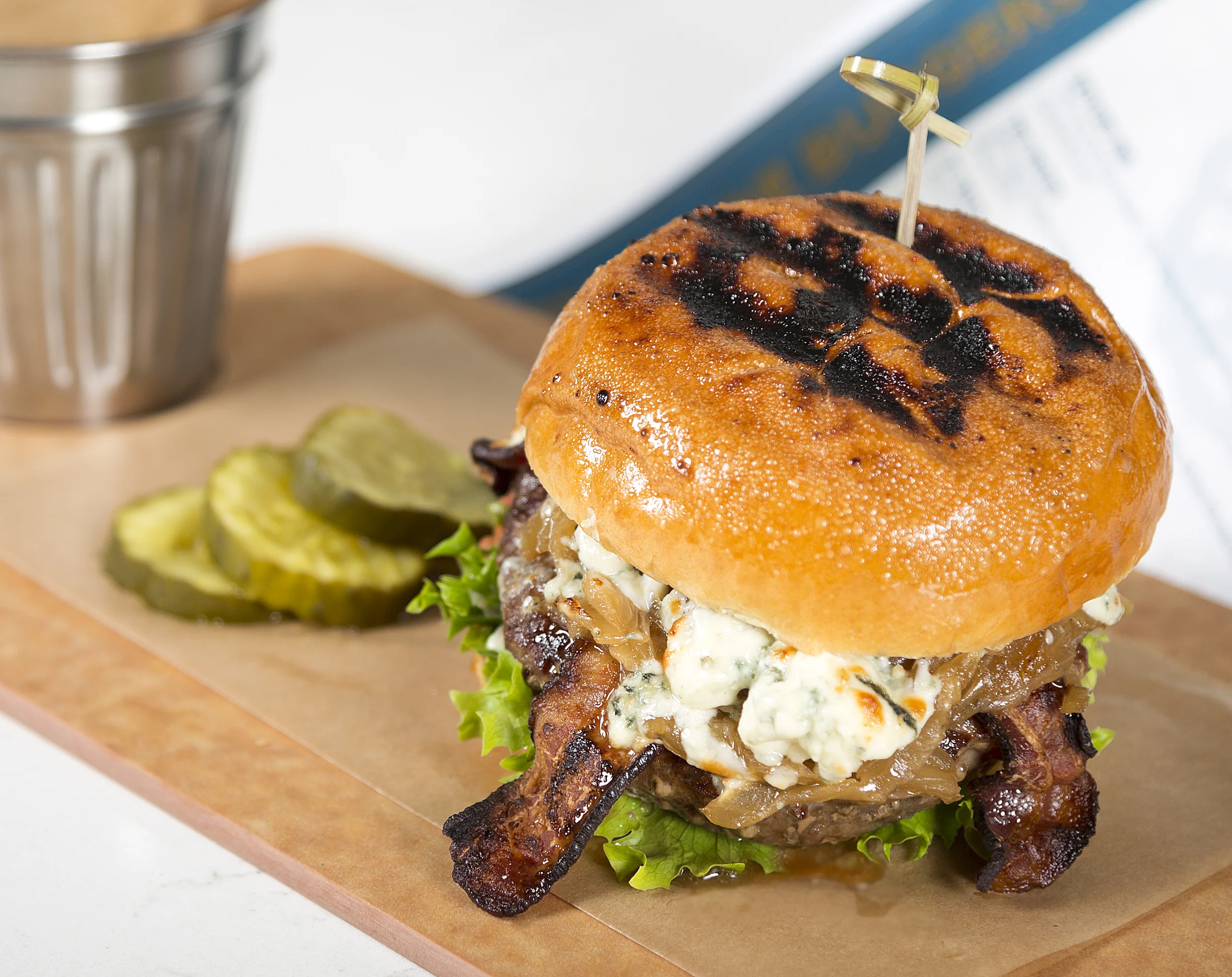BLACK 'N' BLUE Signature Custom Blended Beef Grind, Cajun Spice, Caramelized Onions, Artisan Field Greens, Bacon, Blue Cheese, Garlic Mayo, Toasted Brioche