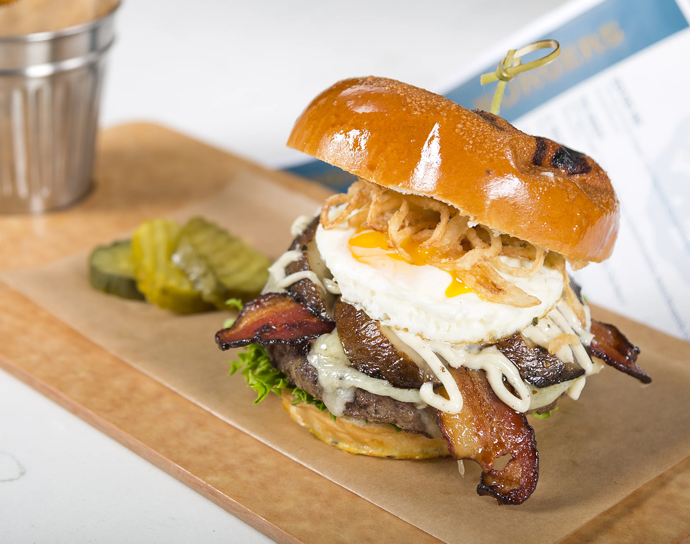 NOONER Signature Custom Blended Beef Grind, Smoked Bacon, Cheddar, Fried Egg, Grilled Portobello Mushroom, Crispy Onions, Field Greens, Garlic Aioli, Toasted Brioche