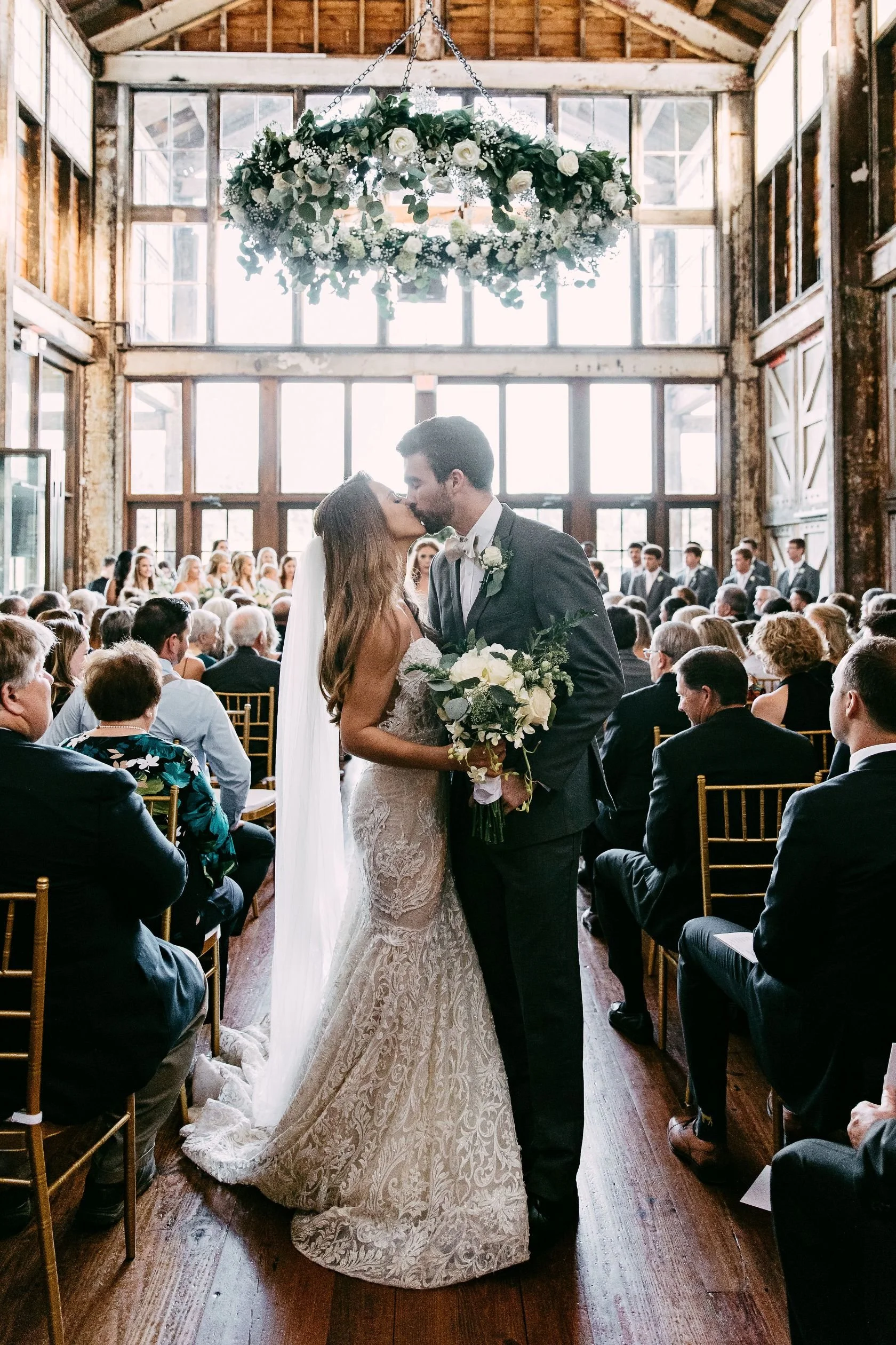 bride and groom kissing under floral chandelier in faulkner room at Jefferson oxford