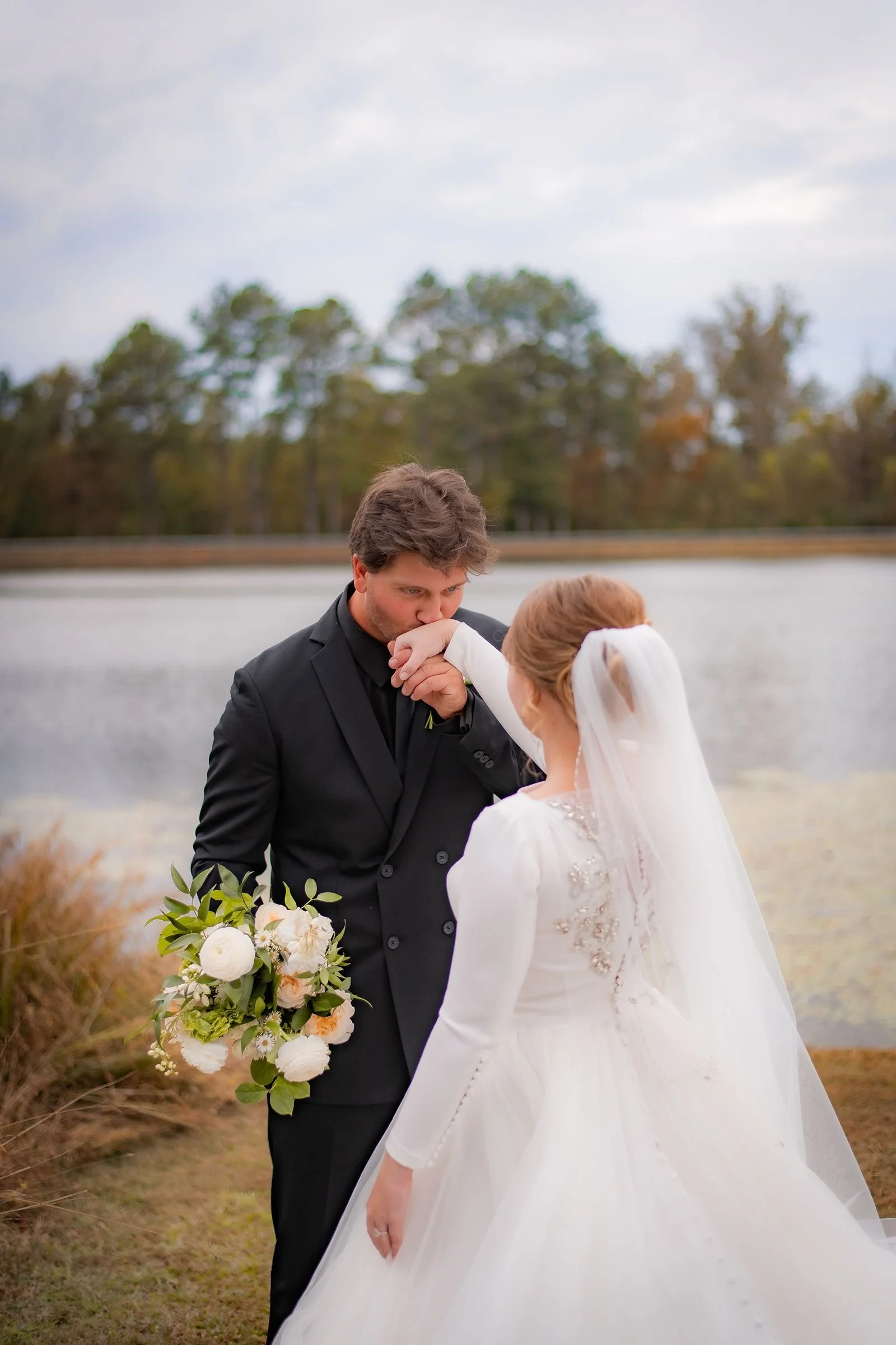 groom kisses brides hand with lake backdrop at Jefferson Oxford MS