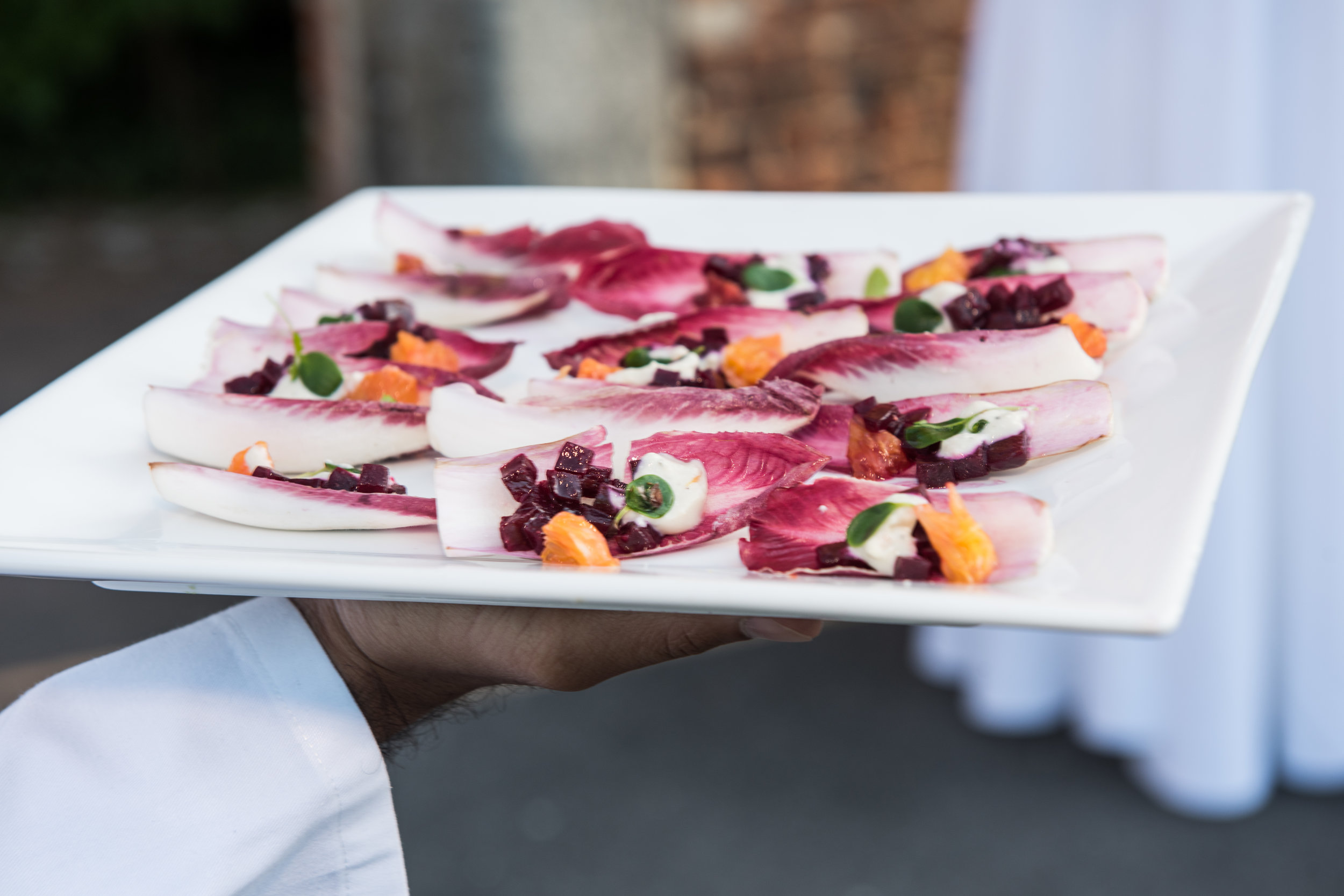A server holding a white platter of red endive leaves topped with colorful vegetables and herbs.
