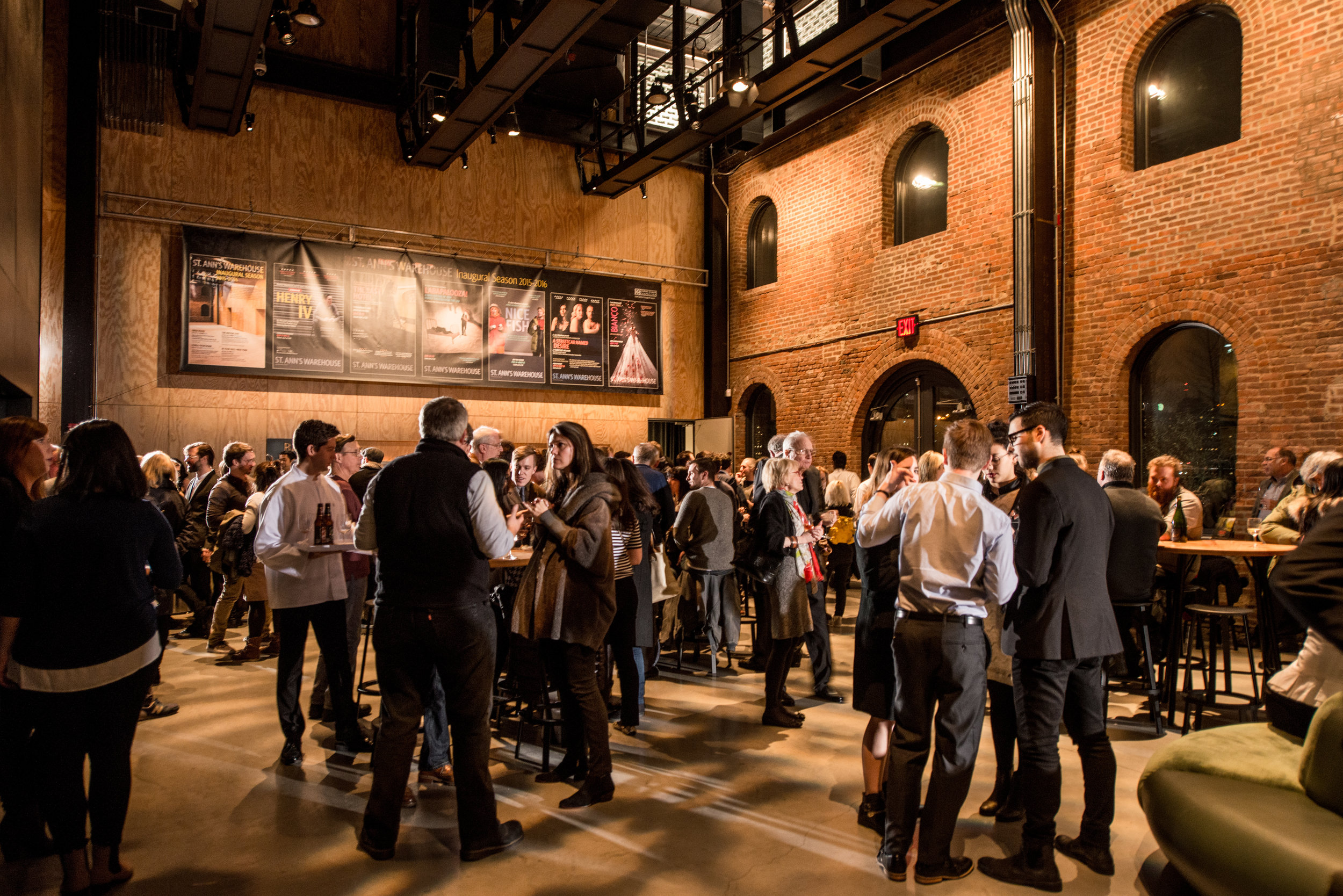 Guests enjoying a cocktail reception in a brick-walled event space with high ceilings.