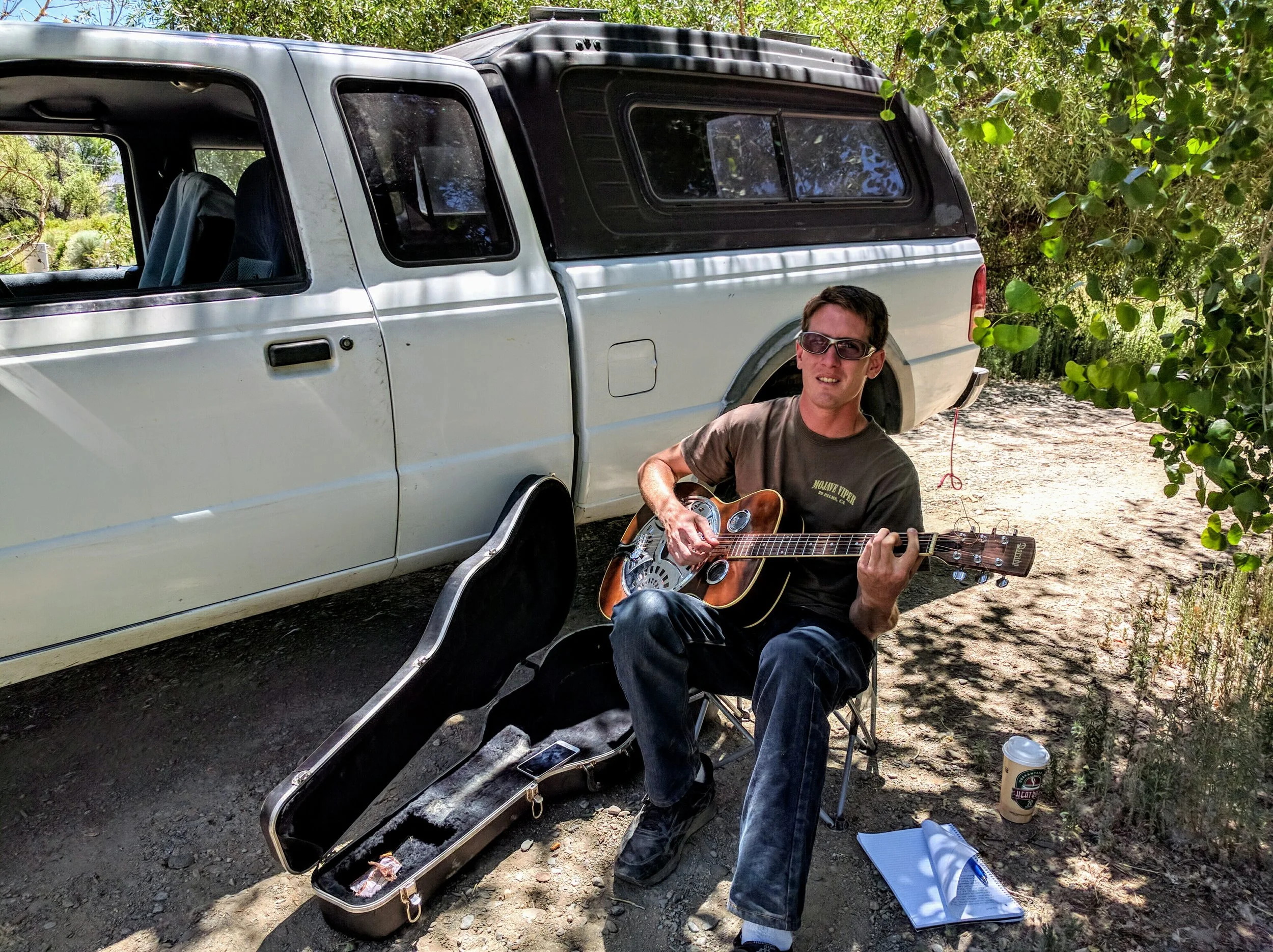 Teddy Ryan playing his guitar under the cool shade of a tree along the canal.